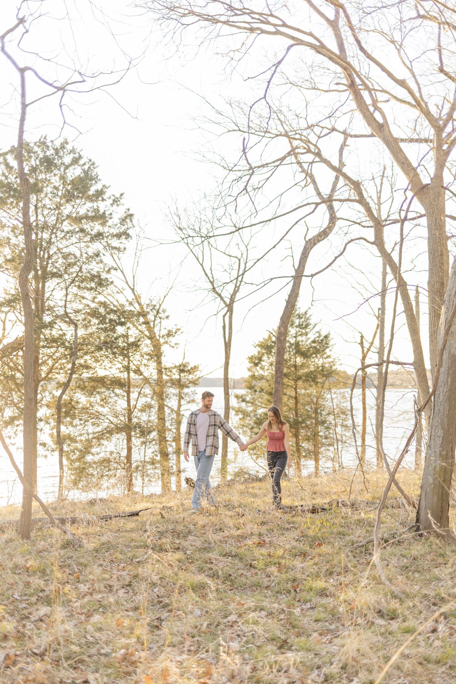 A couple stands together in a wooded area during golden hour with sunlight filtering through trees in Raleigh, North Carolina.