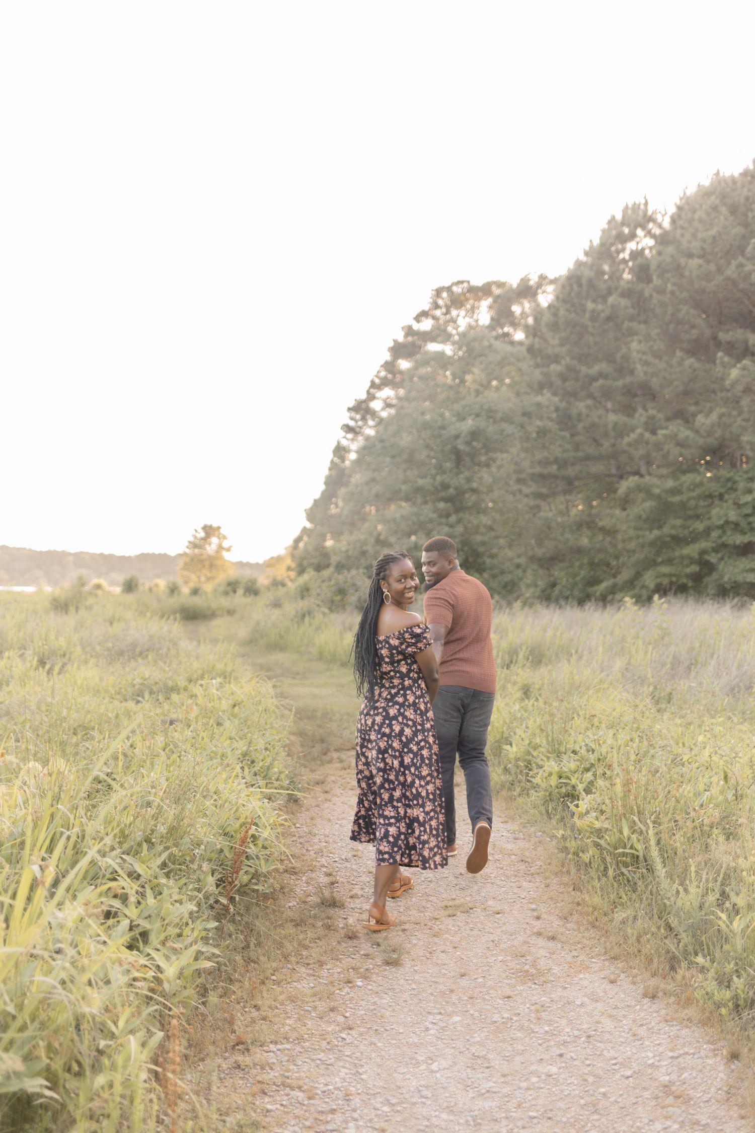 Romantic couple sharing a tender moment on a nature path, woman in floral dress smiling at camera.