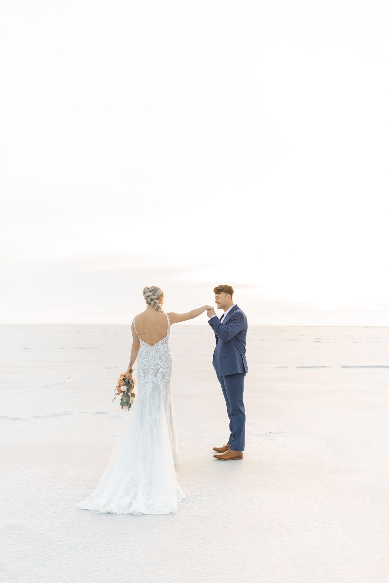A couple shares their first look moment at a bright outdoor wedding venue with the bride in a backless lace gown.