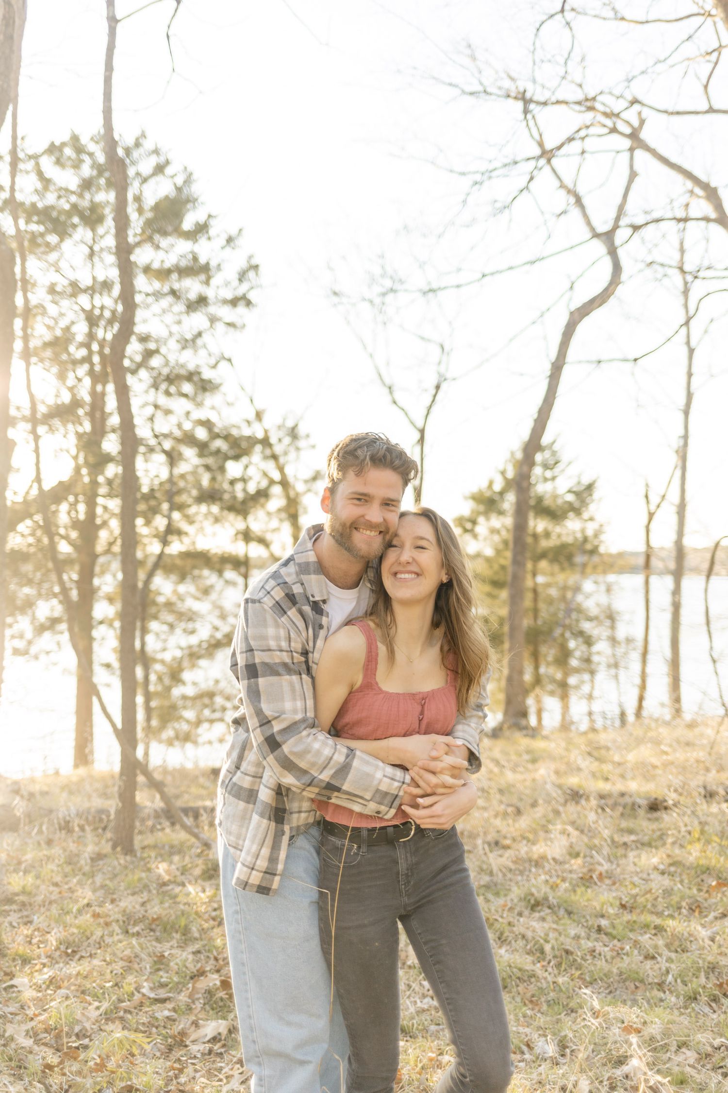Couple sharing playful moments on a hillside with pine trees during sunset during photoshoot with Kinsley Nicole Photography.