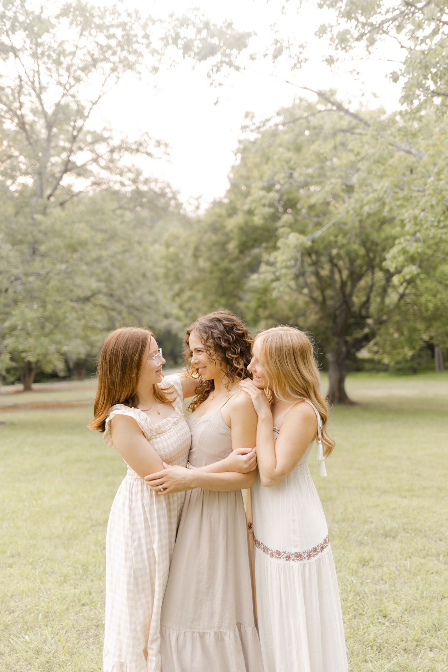 A group shares a tender moment together in light summer dresses on a grassy field with Durham, North Carolina Photographer.
