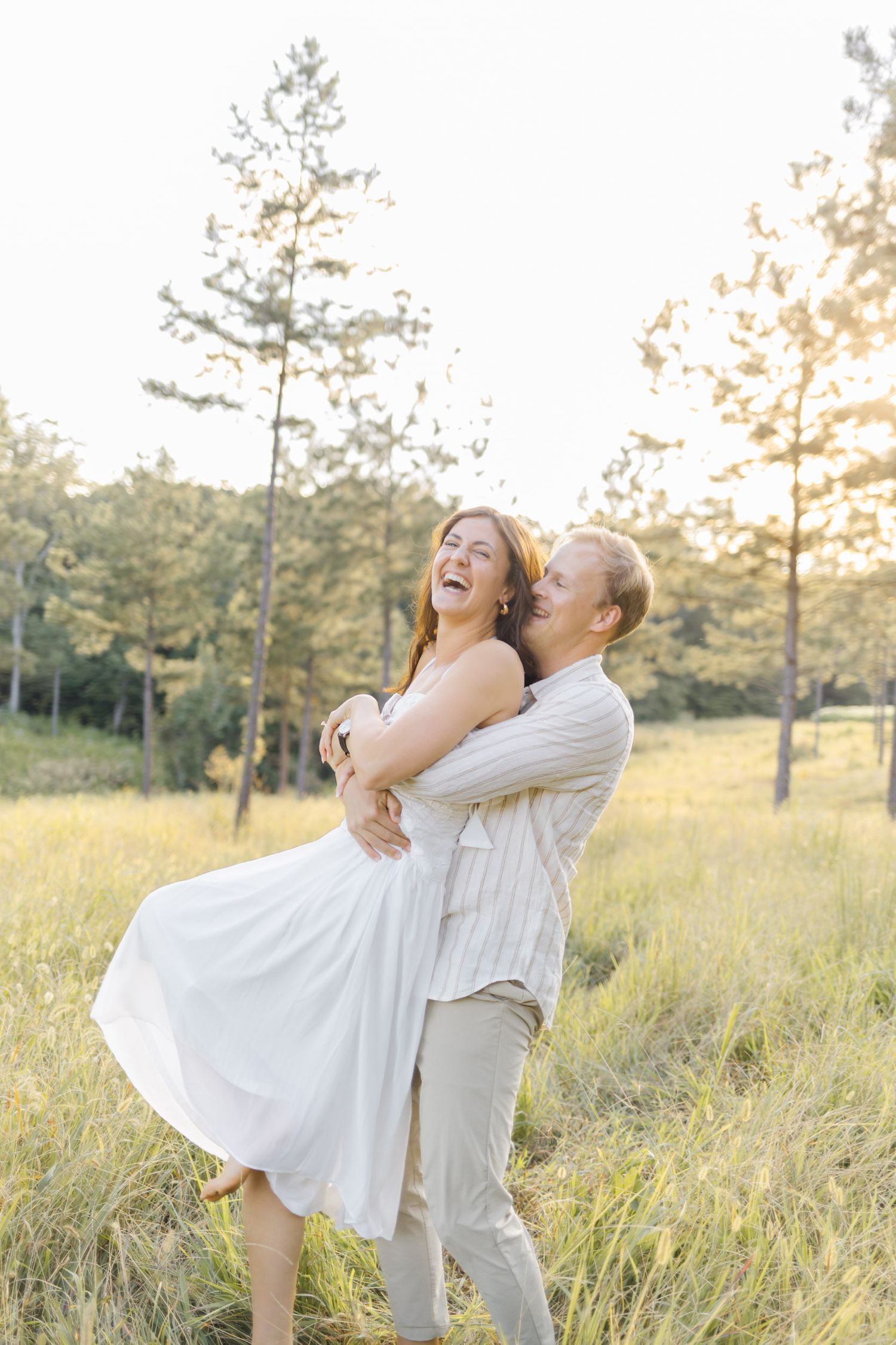 Joyful couple embracing and spinning in a golden meadow during sunset making a light, airy, creamy photo.