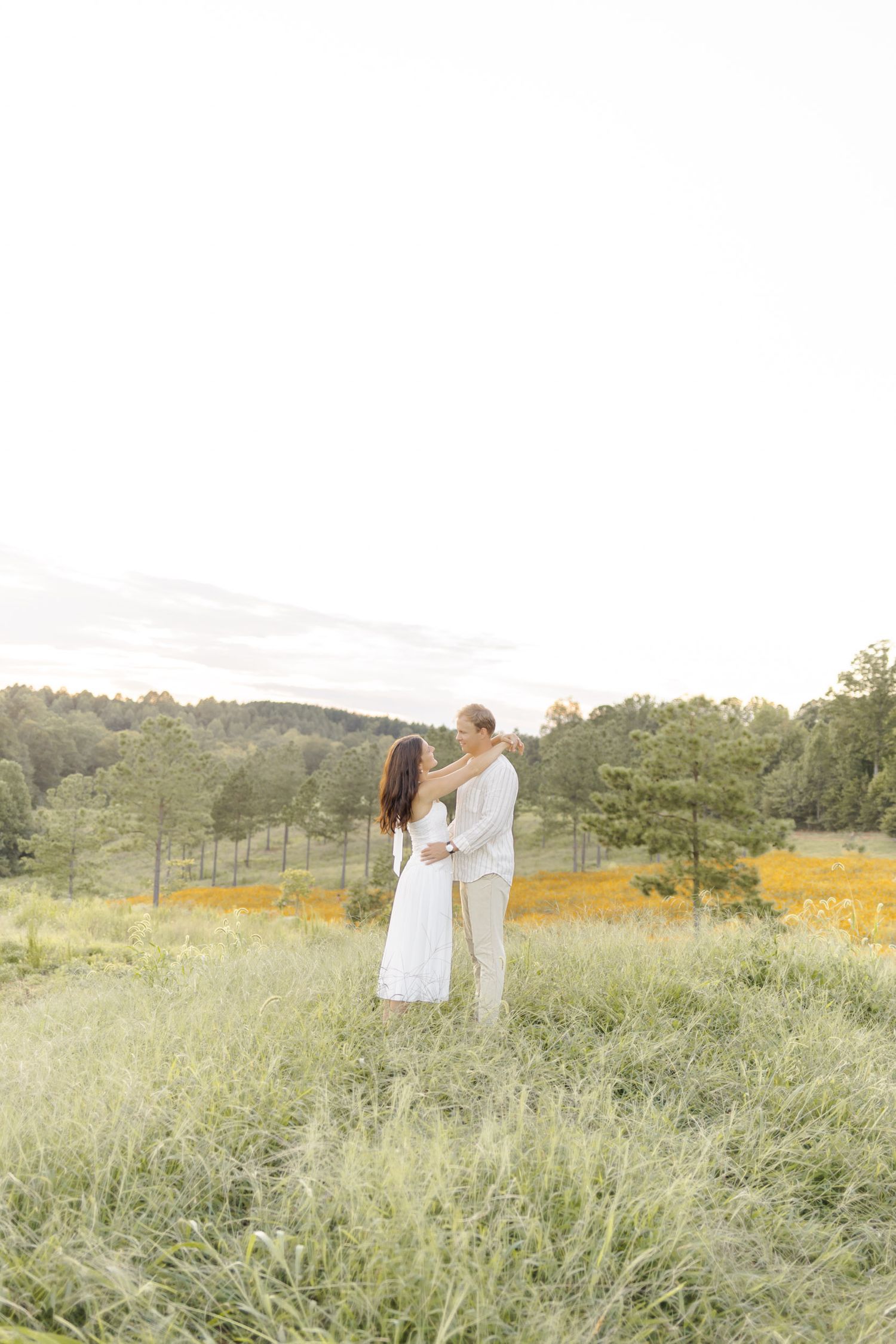Couple embracing in golden light among wildflowers and tall grass during engagement session with photographer in North Carolina.