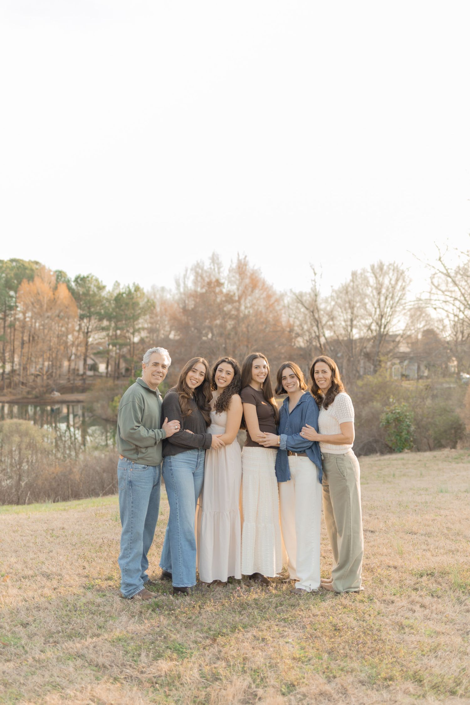 Family of six posing together outdoors near a pond during golden hour in a field with autumn trees.