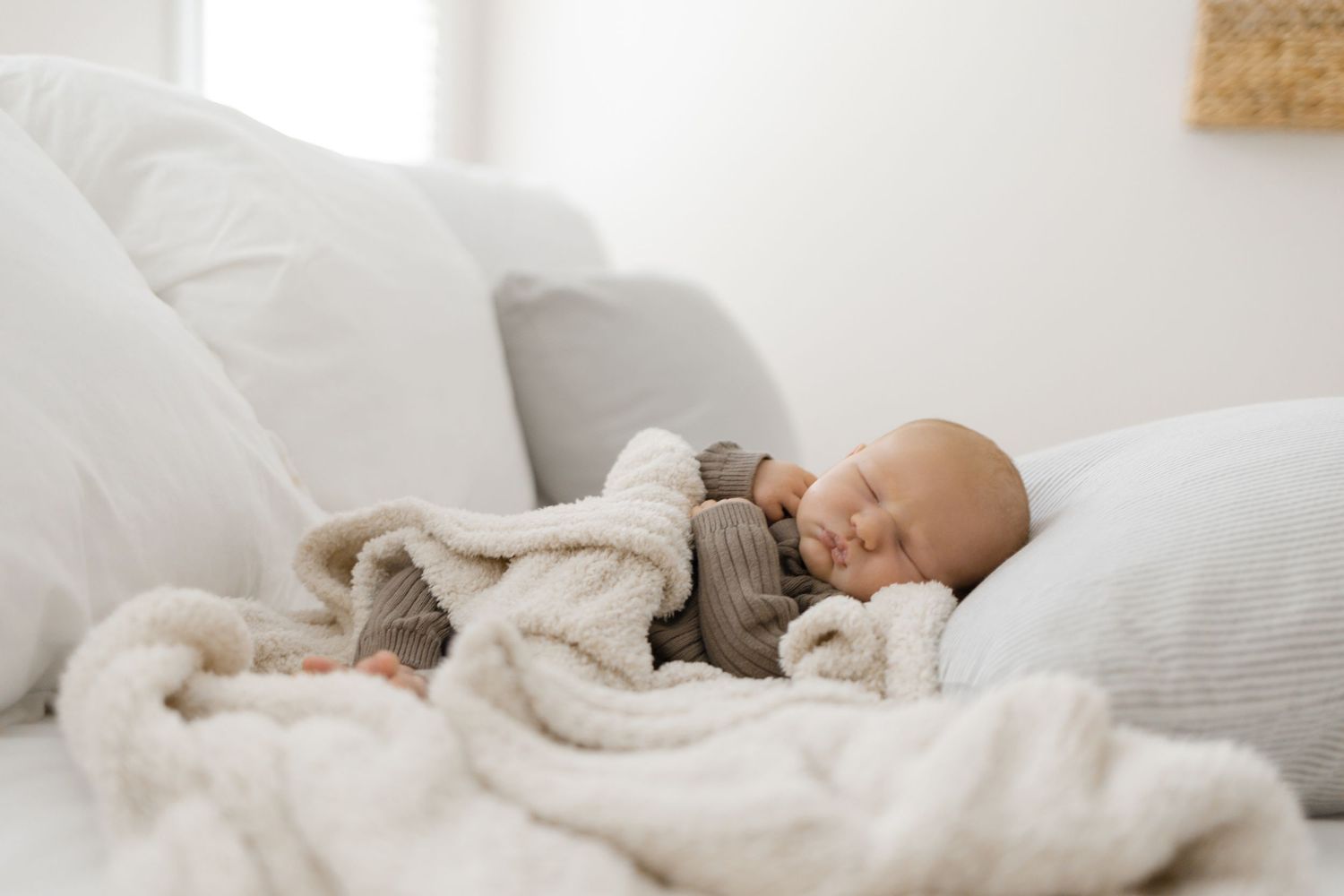 Peaceful sleeping baby wrapped in cozy white blankets and wearing gray clothing on soft bedding.