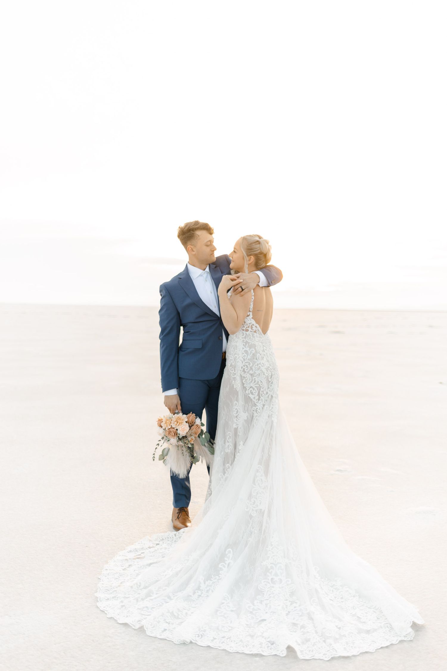 Wedding couple in blue suit and lace dress photographed on bright white terrain.
