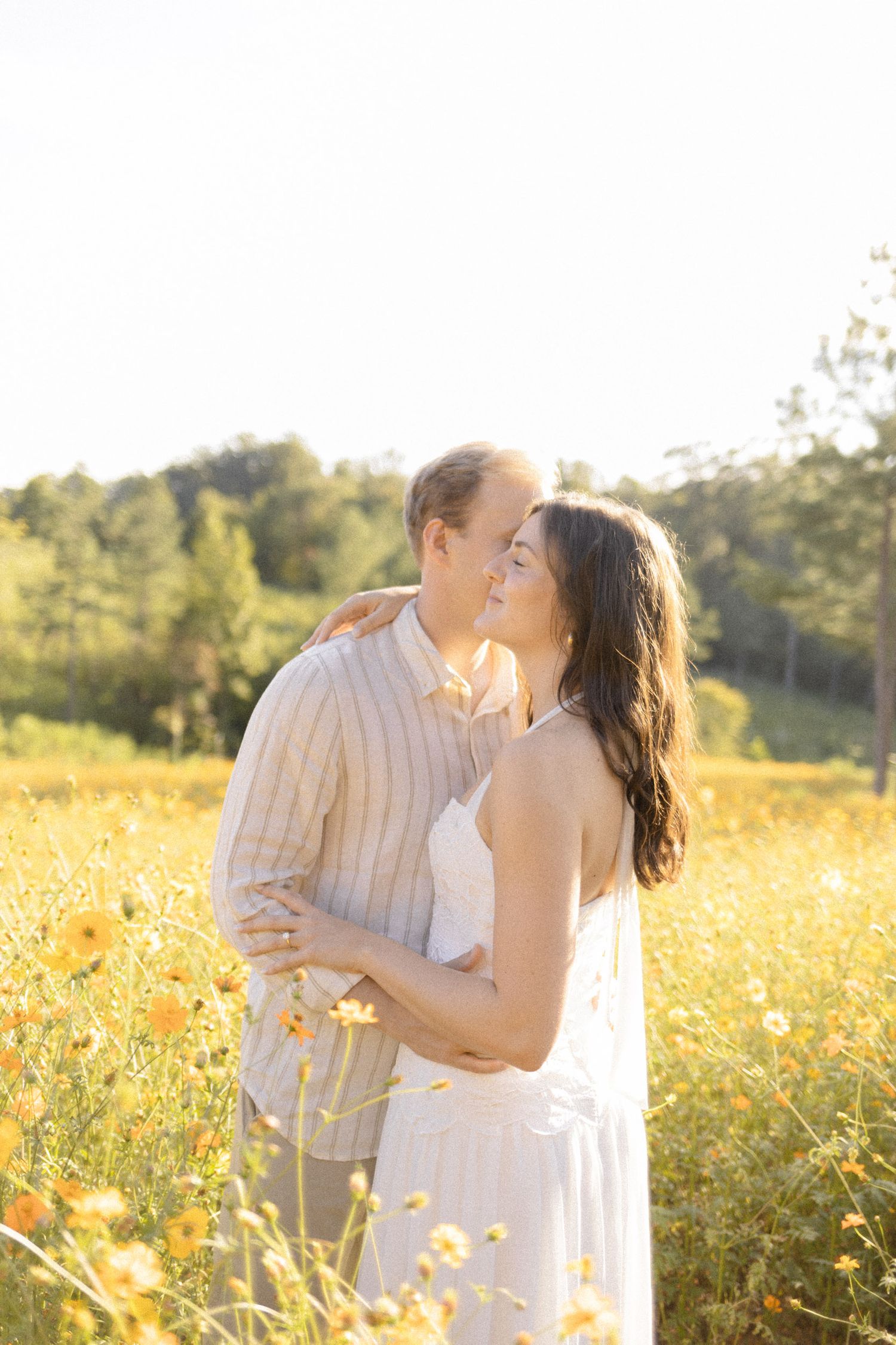 Intimate moment between couple in white clothing surrounded by yellow wildflowers at sunset during lifestyle portrait photoshoot.