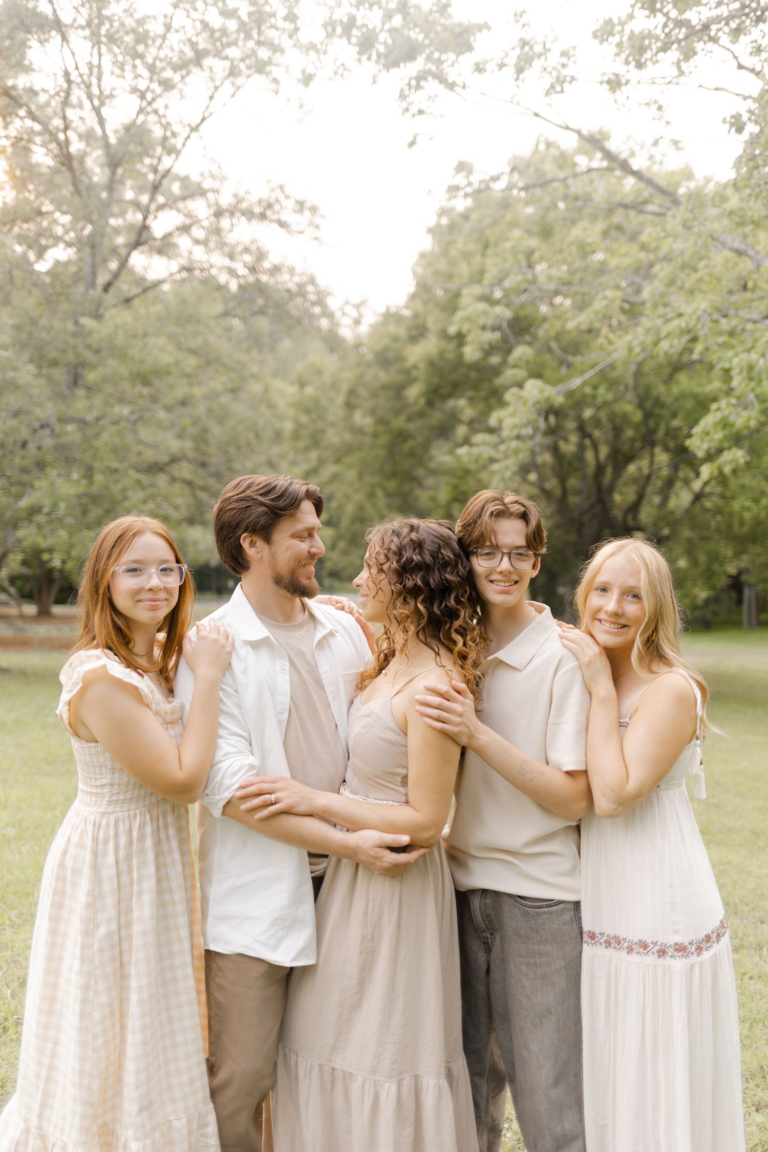 Candid group photo showing friends laughing and embracing in a sunlit park.