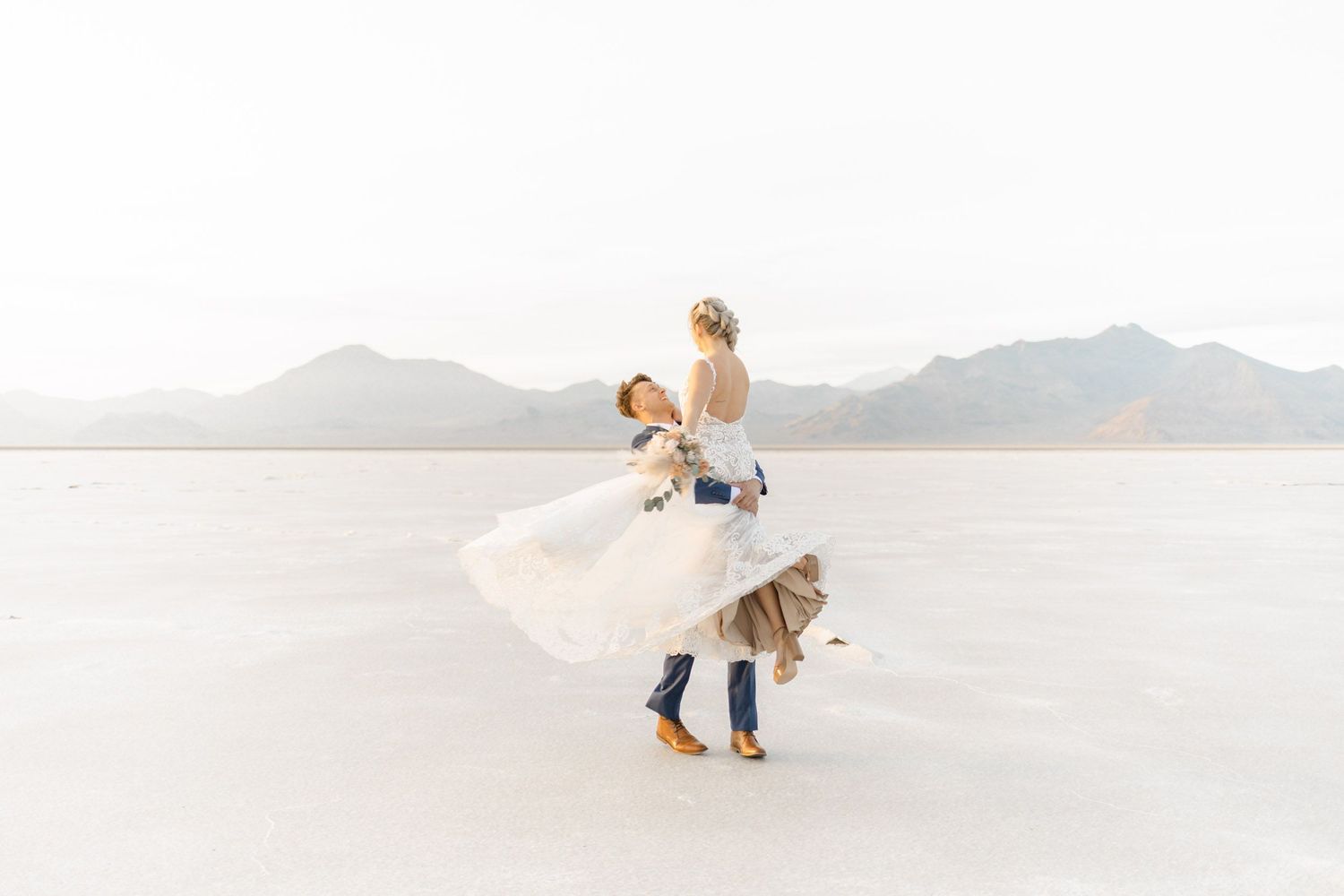 Newlyweds share a romantic moment while dancing on a scenic salt flat with mountains in the distance.