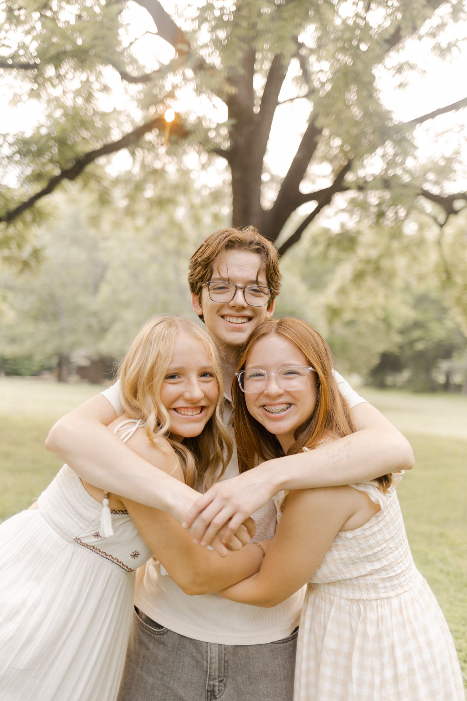 Two friends share joyful hugs and laughter in a sunny outdoor setting wearing light summer dresses while doing a photoshoot.