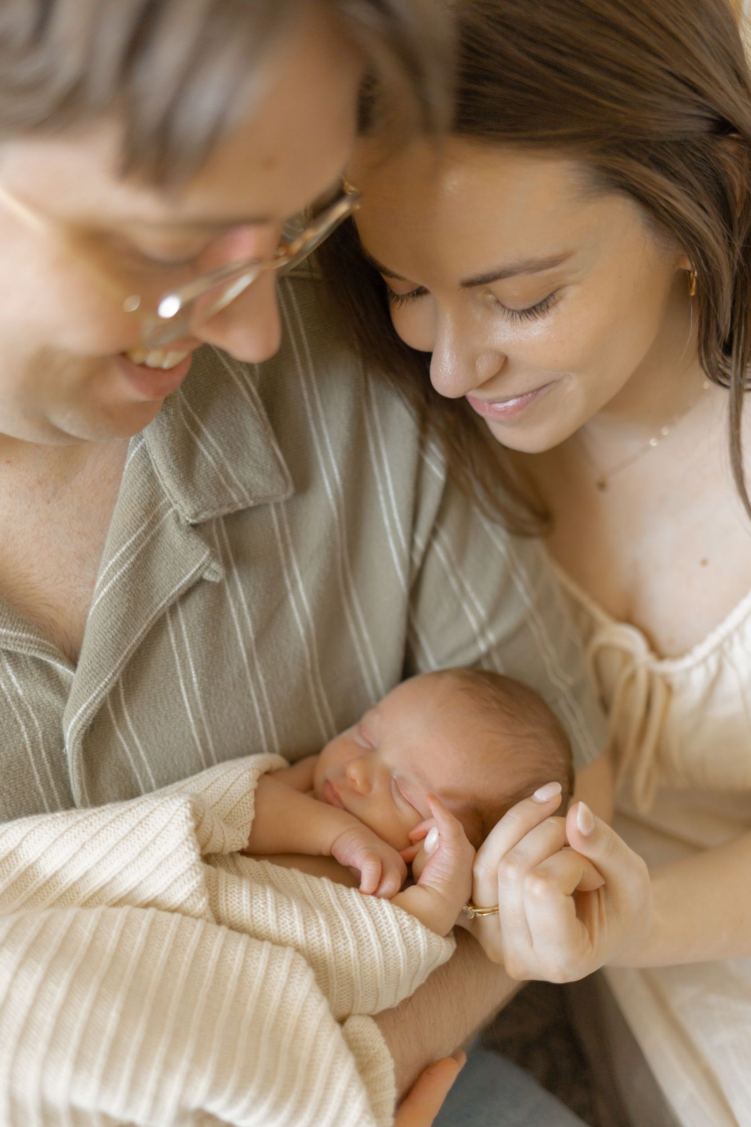Two smiling mothers tenderly gazing at their sleeping newborn baby wrapped in a cream knit blanket.