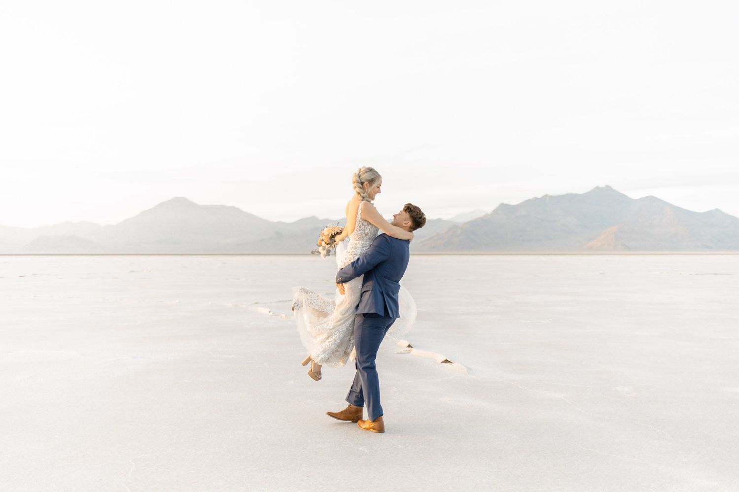 Newlyweds dance together on a scenic salt flats with mountains in the background at sunset.