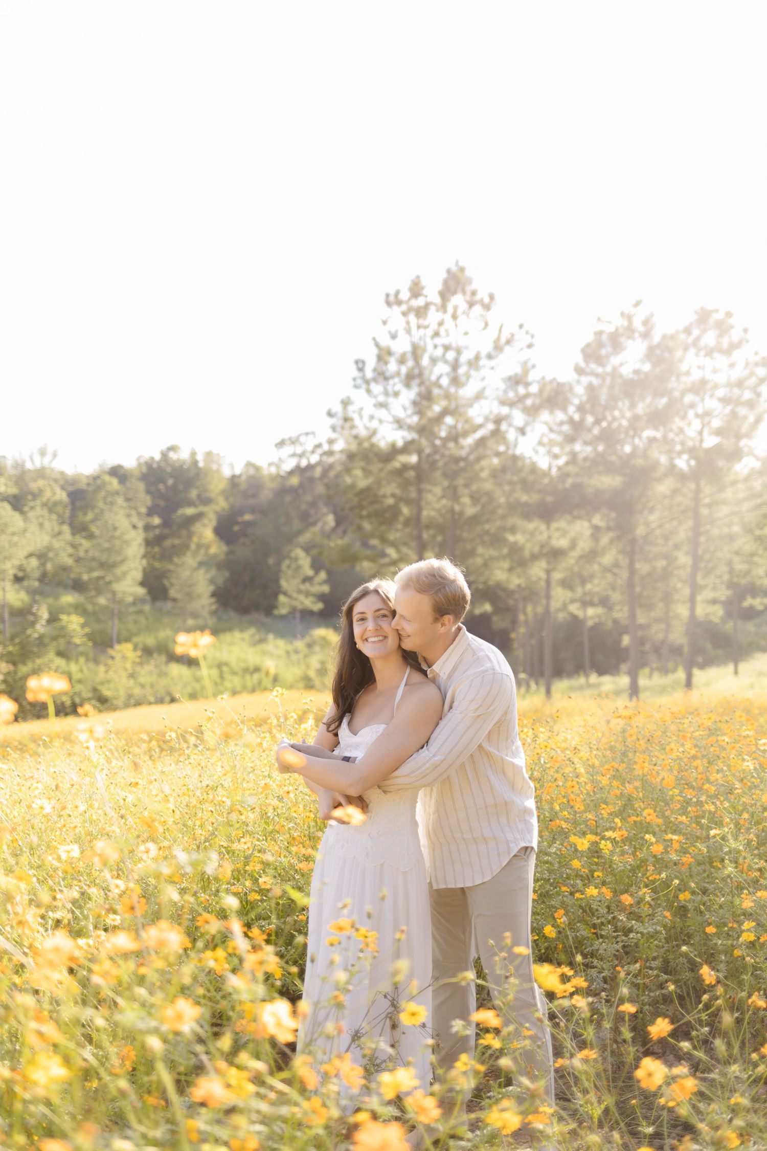 Couple shares tender moments while walking through a meadow of yellow flowers during golden hour for engagement photoshoot in Chapel Hill.
