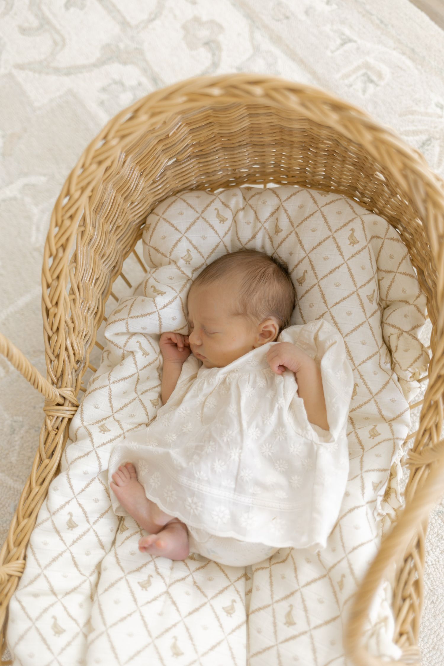 Newborn baby sleeping peacefully in a wicker Moses basket with white bedding.