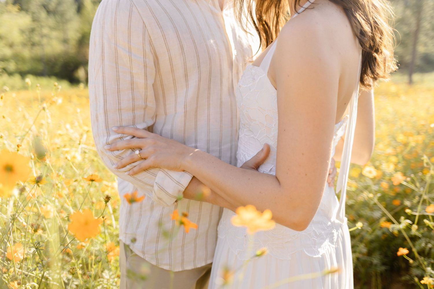 Intimate moment captured between a couple in white clothing among golden flowers at sunset for engagement photoshoot in Chapel Hill, NC.