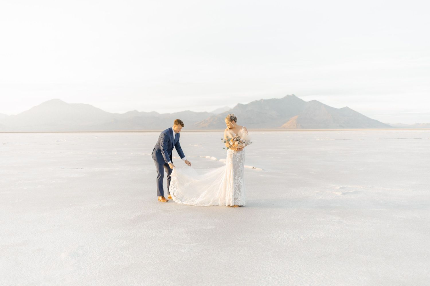 Couple walking and posing together on vast white salt flats with mountains in the distance.
