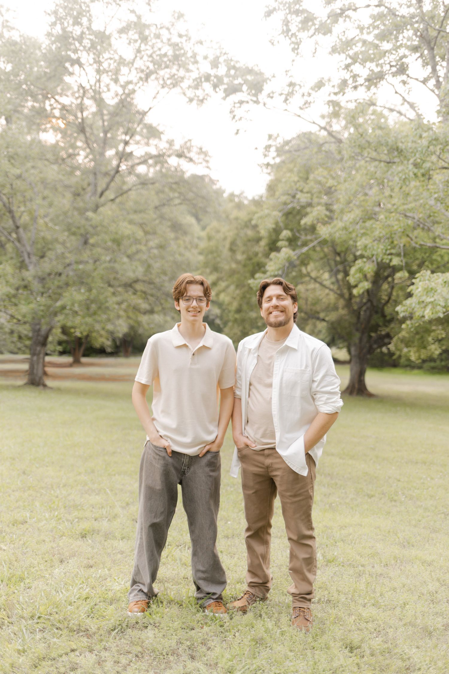 Two people in casual attire stand together smiling in a grassy field on a bright day with Durham, North Carolina Photographer.