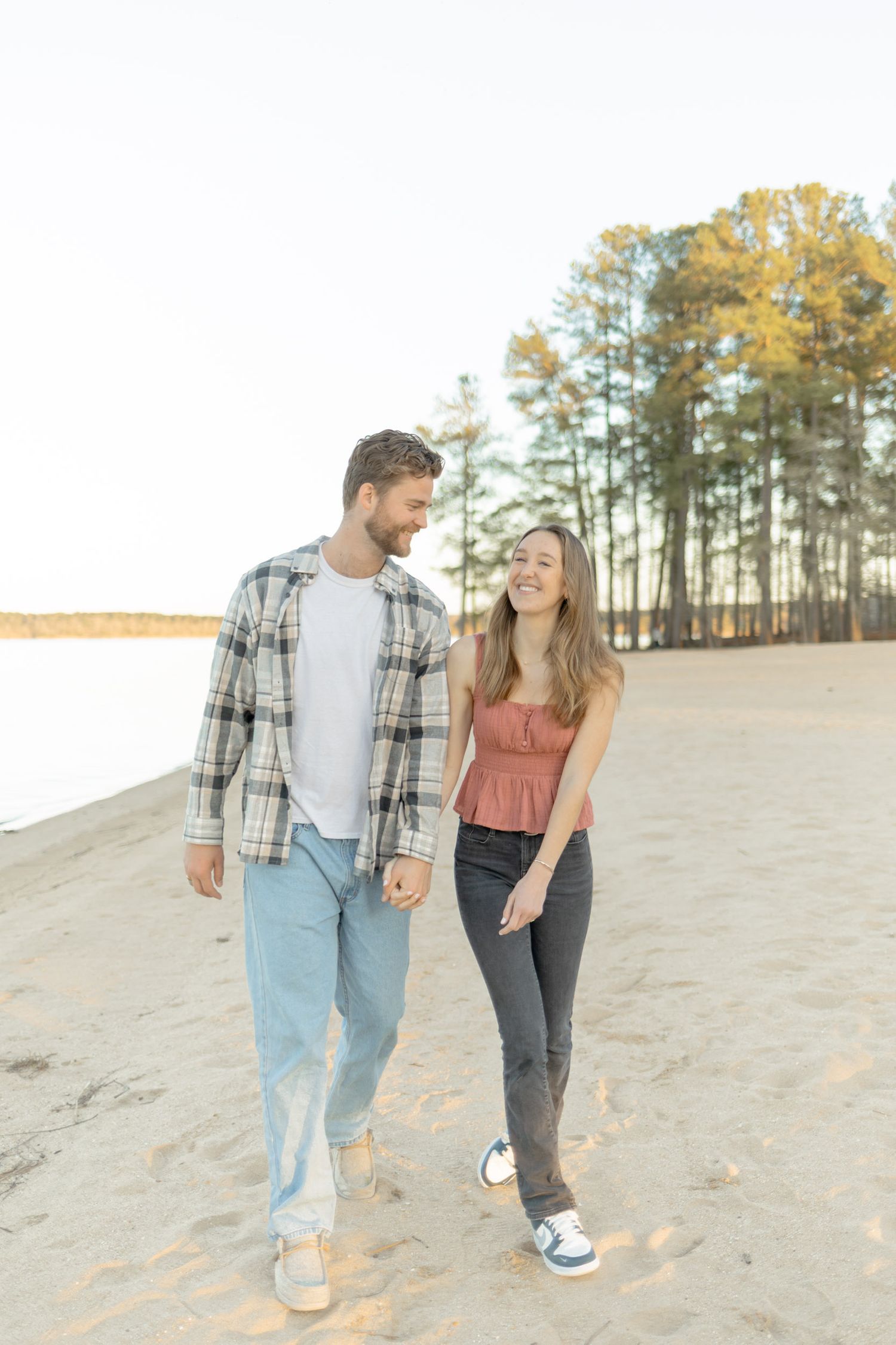 Couple walking hand in hand on sandy terrain with pine trees in background during photoshoot with Kinsley Nicole Photography.