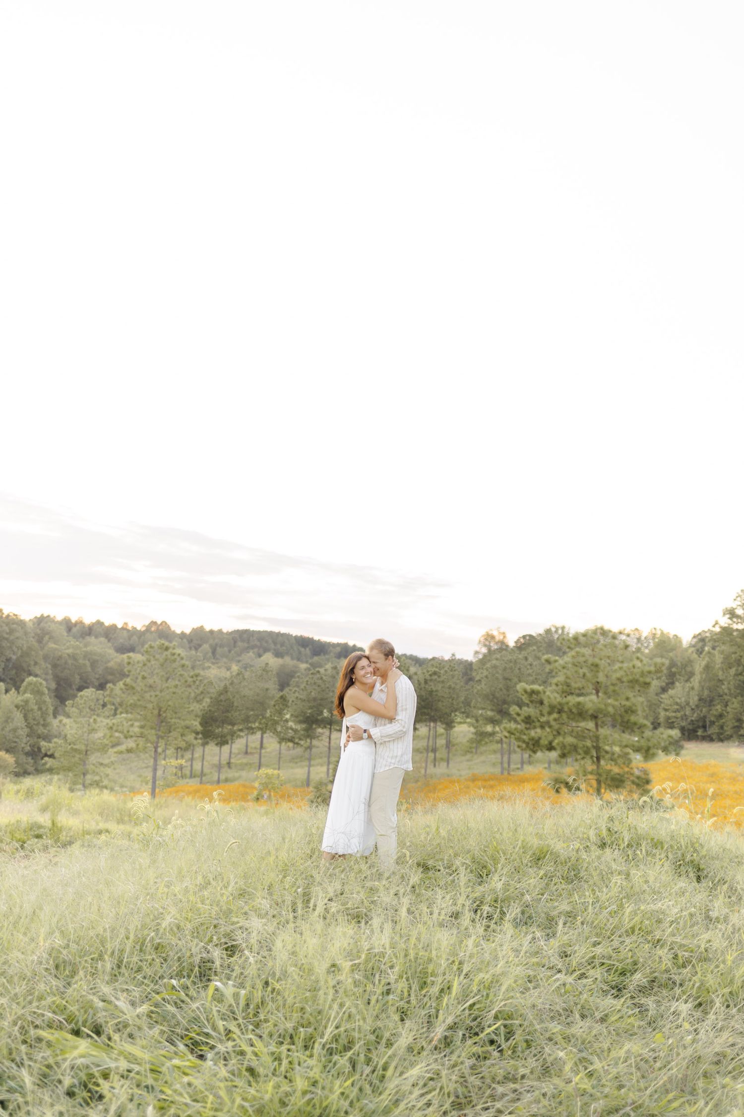 Couple sharing tender moment in summer meadow during golden hour during engagement session in Chapel Hill, NC.