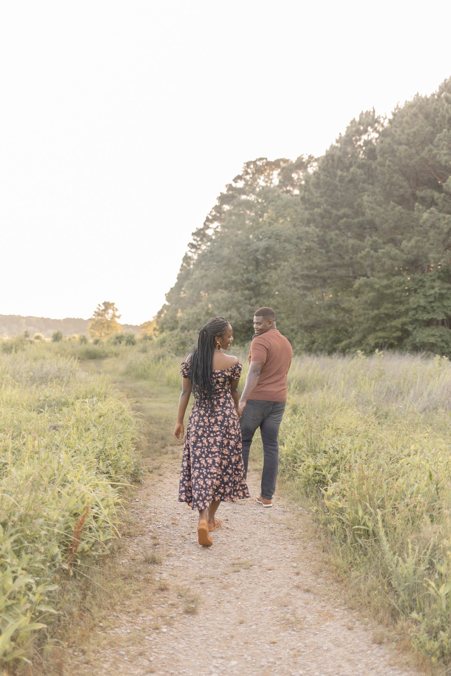 Couple walking hand-in-hand on a scenic path through lush green fields at golden hour sunset.