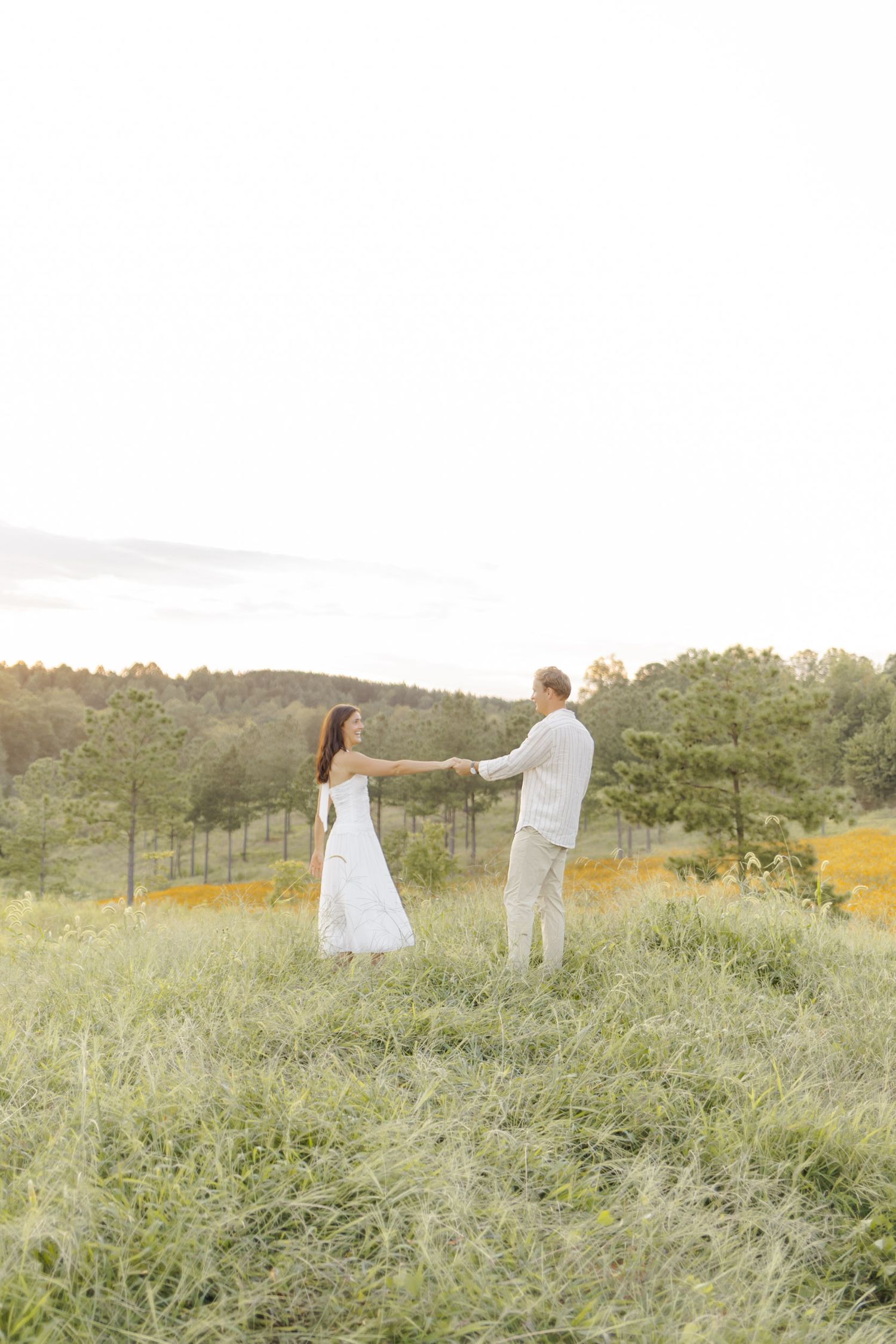 A couple dances in a hilltop meadow surrounded by golden wildflowers during engagement session in Chapel Hill, NC.