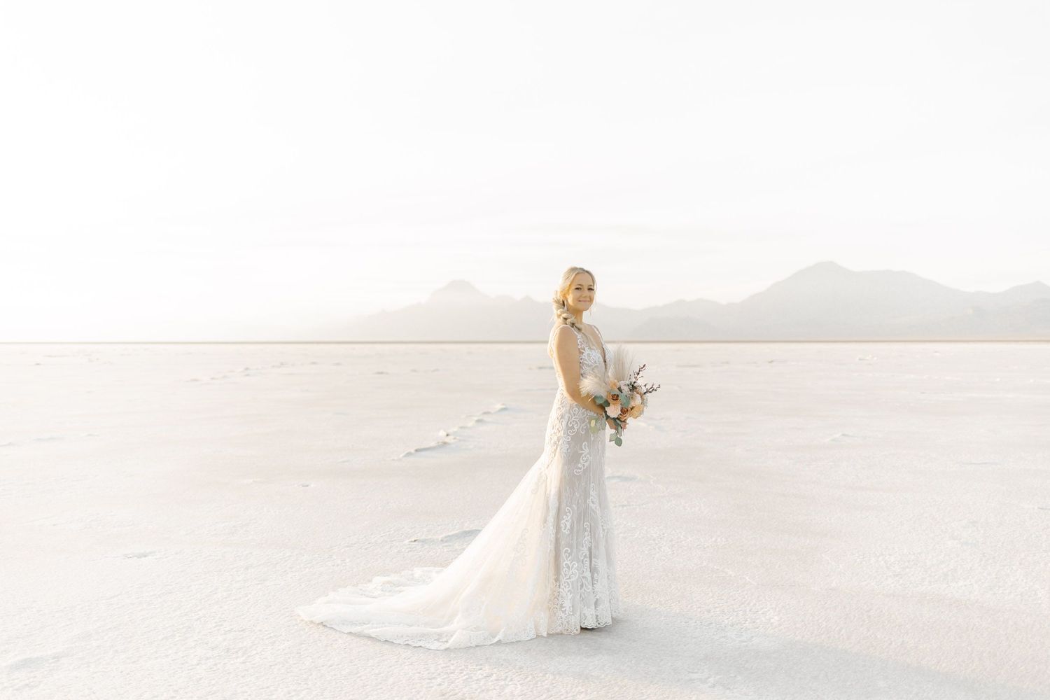 A bride and groom share an intimate moment on a sandy beach with soft white waves in the background.