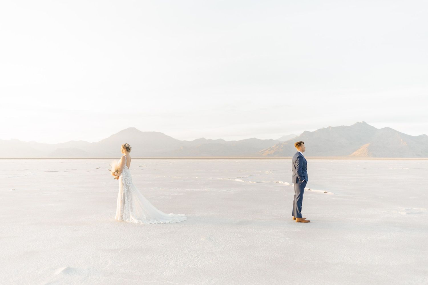 Wedding couple poses artistically on Bonneville Salt Flats with dramatic mountain backdrop at sunset.
