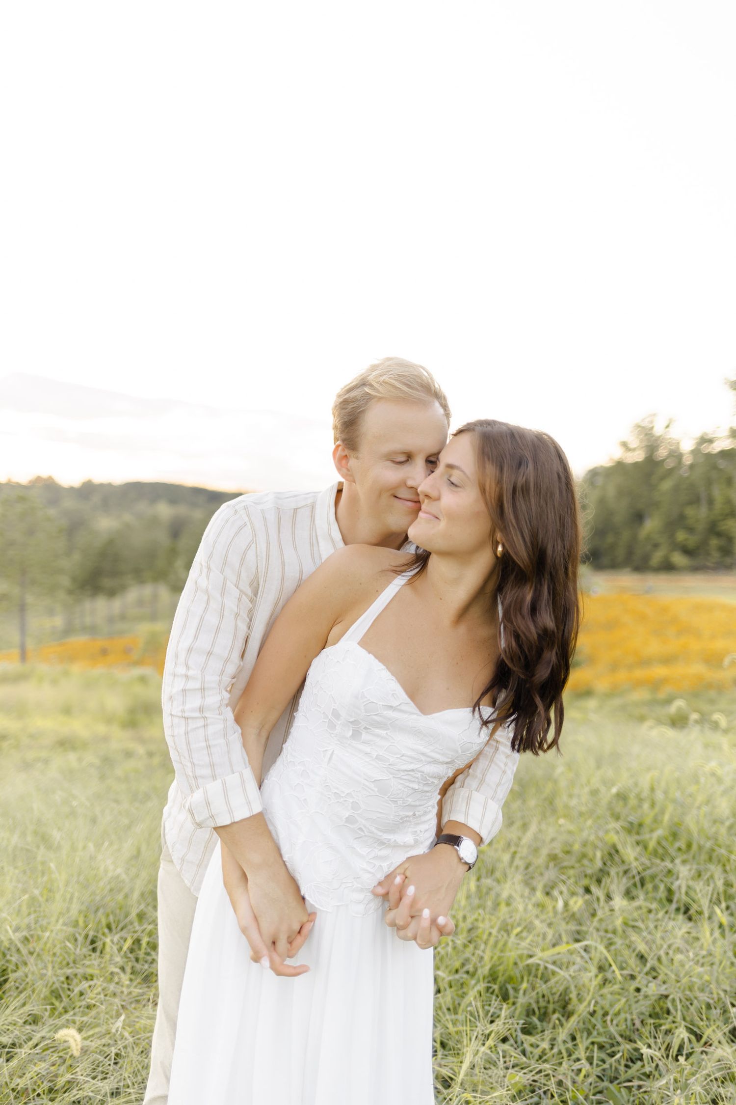 A tender moment between a couple in white attire against a natural outdoor setting during engagement session in Chapel Hill, NC.