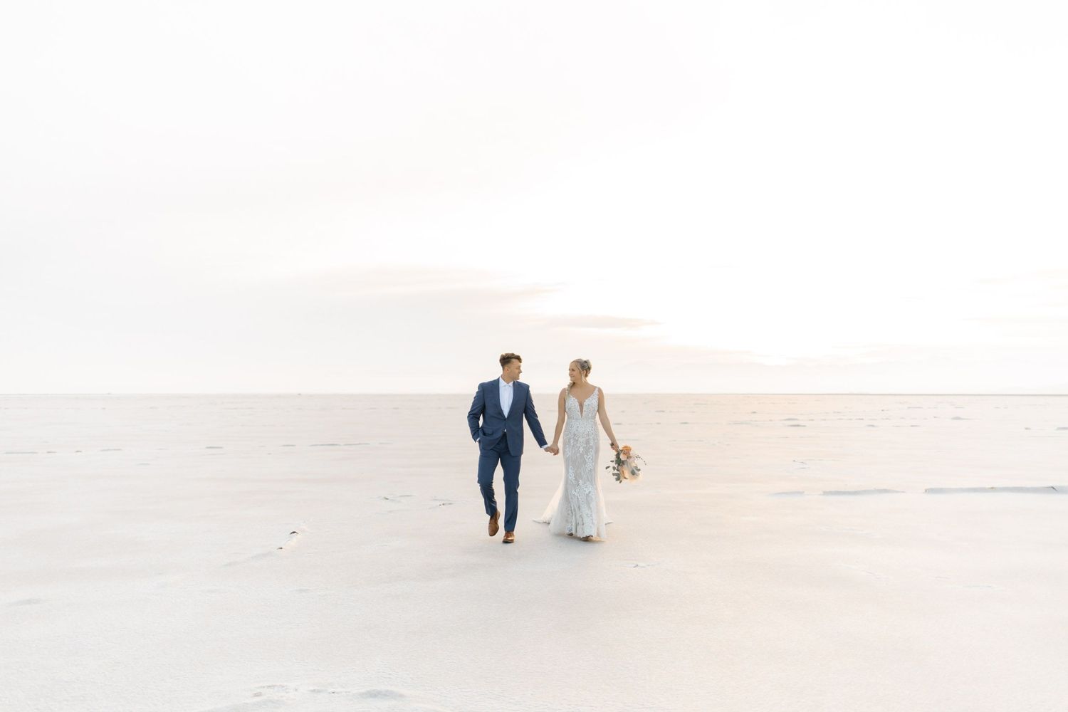 A couple walks hand in hand along a serene beach shoreline during a peaceful sunset moment.