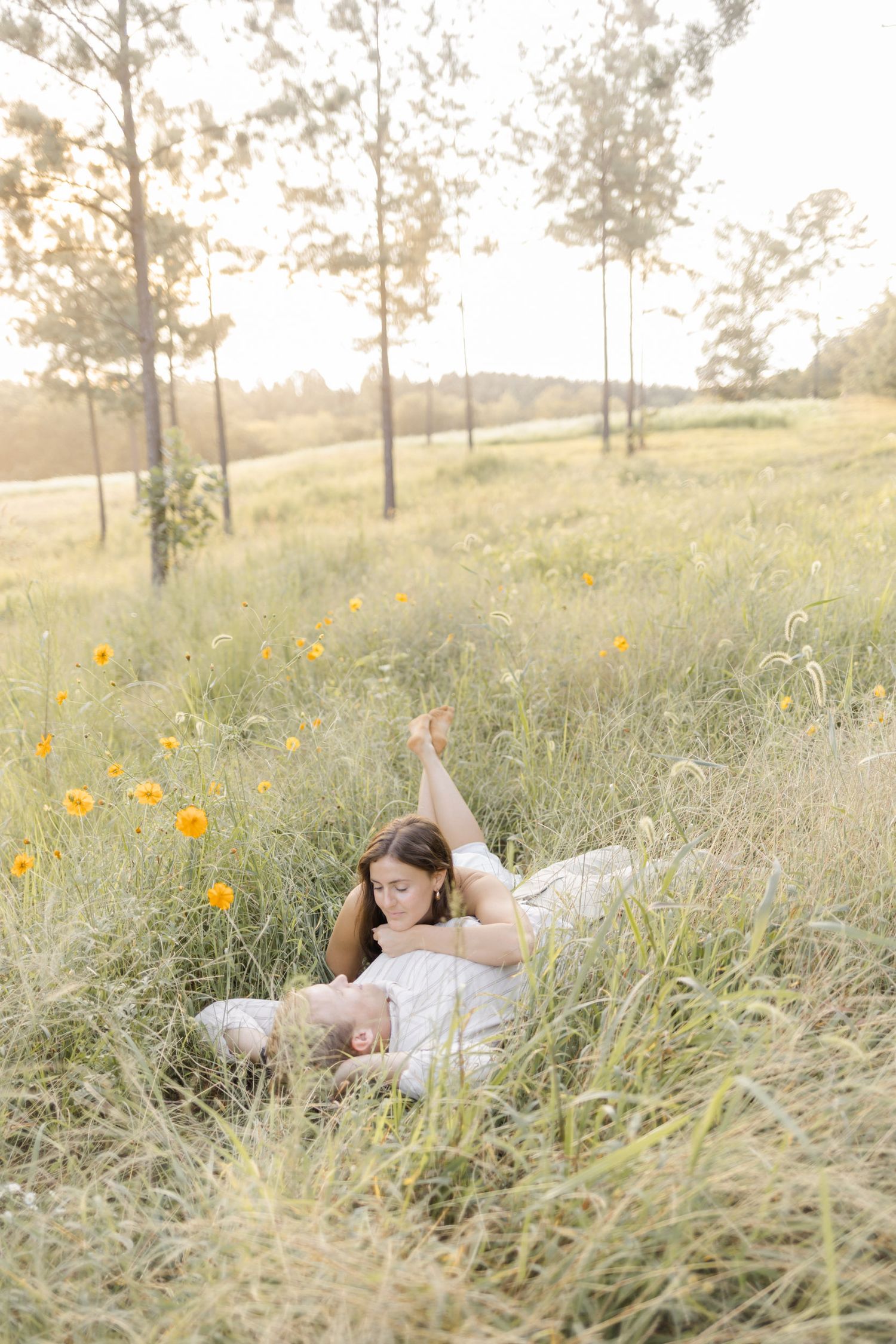 Couple resting peacefully in tall grass surrounded by yellow flowers making a light, airy, creamy photo.