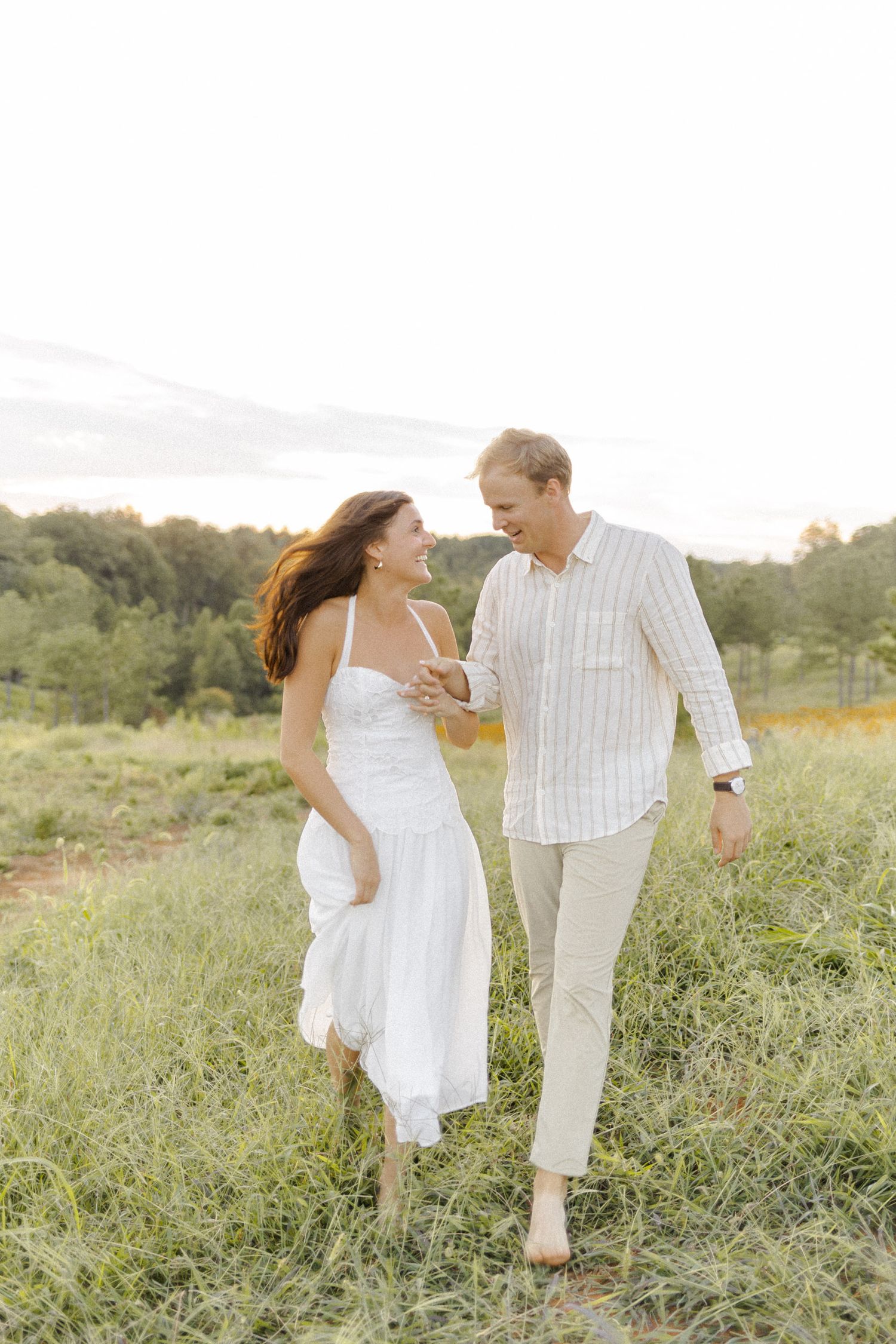 A couple shares a playful moment while walking through tall grass in a field during engagement session in Chapel Hill, NC.