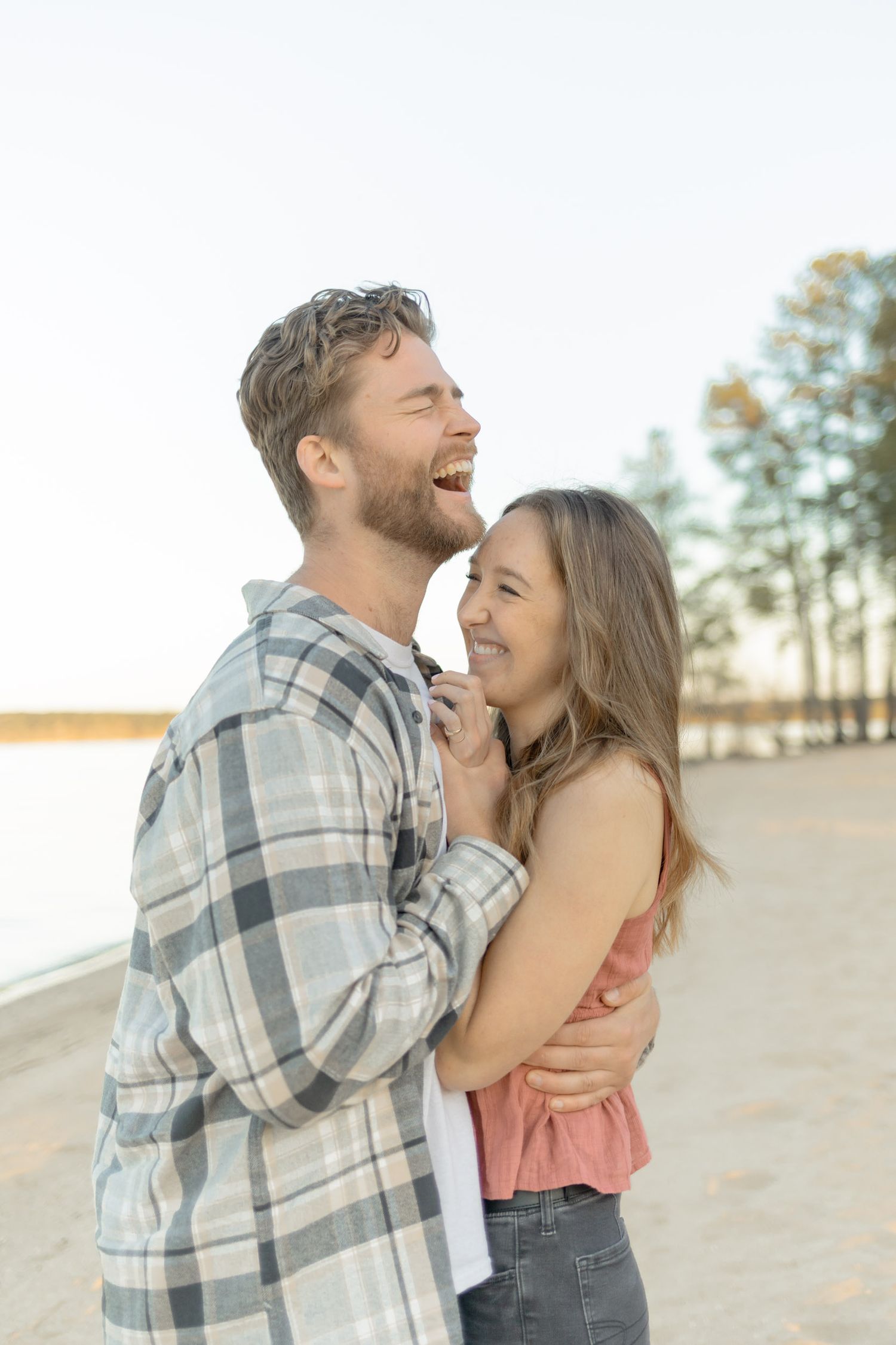 Happy couple laughing and embracing on a sandy slope during golden hour in Raleigh, North Carolina.