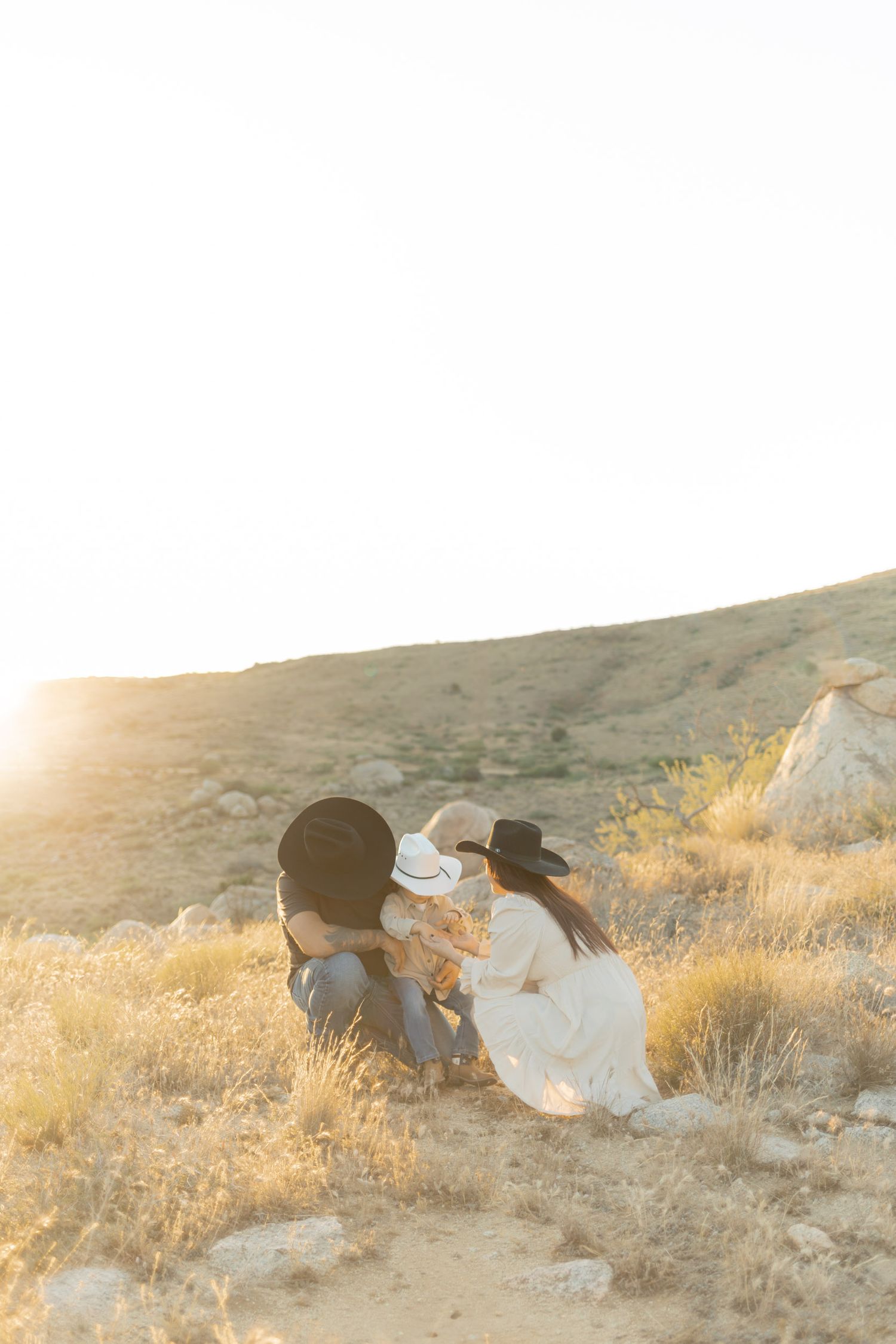 Family with cowboy hats sitting together in golden desert landscape at sunset.