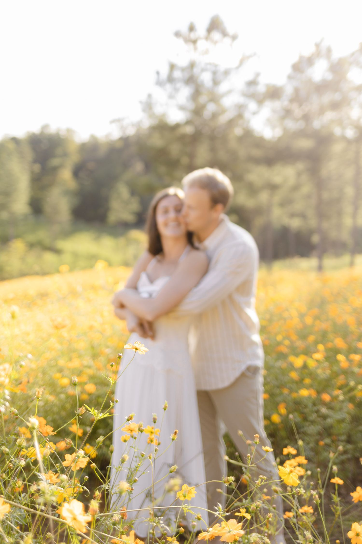 Romantic couple in white embracing among yellow wildflowers during golden hour for engagement photoshoot in Chapel Hill, NC.