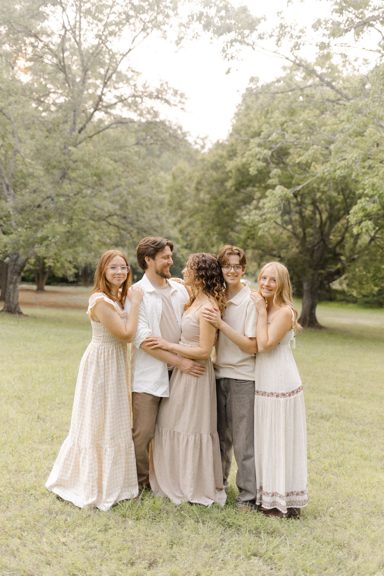 Friends wearing coordinated neutral tones embrace while standing in a sunny park.