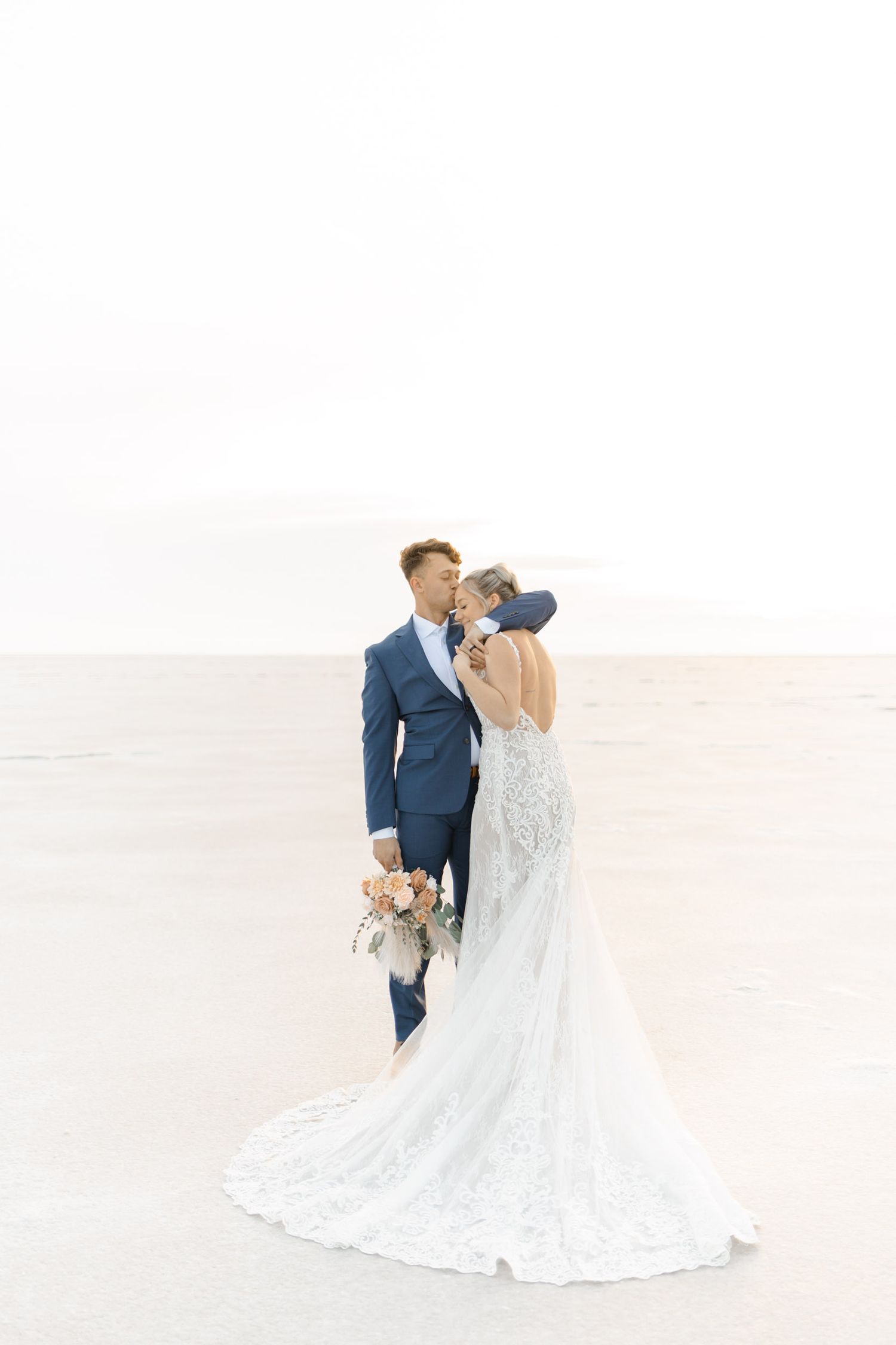 Bride and groom share intimate moment on vast white salt flats landscape.