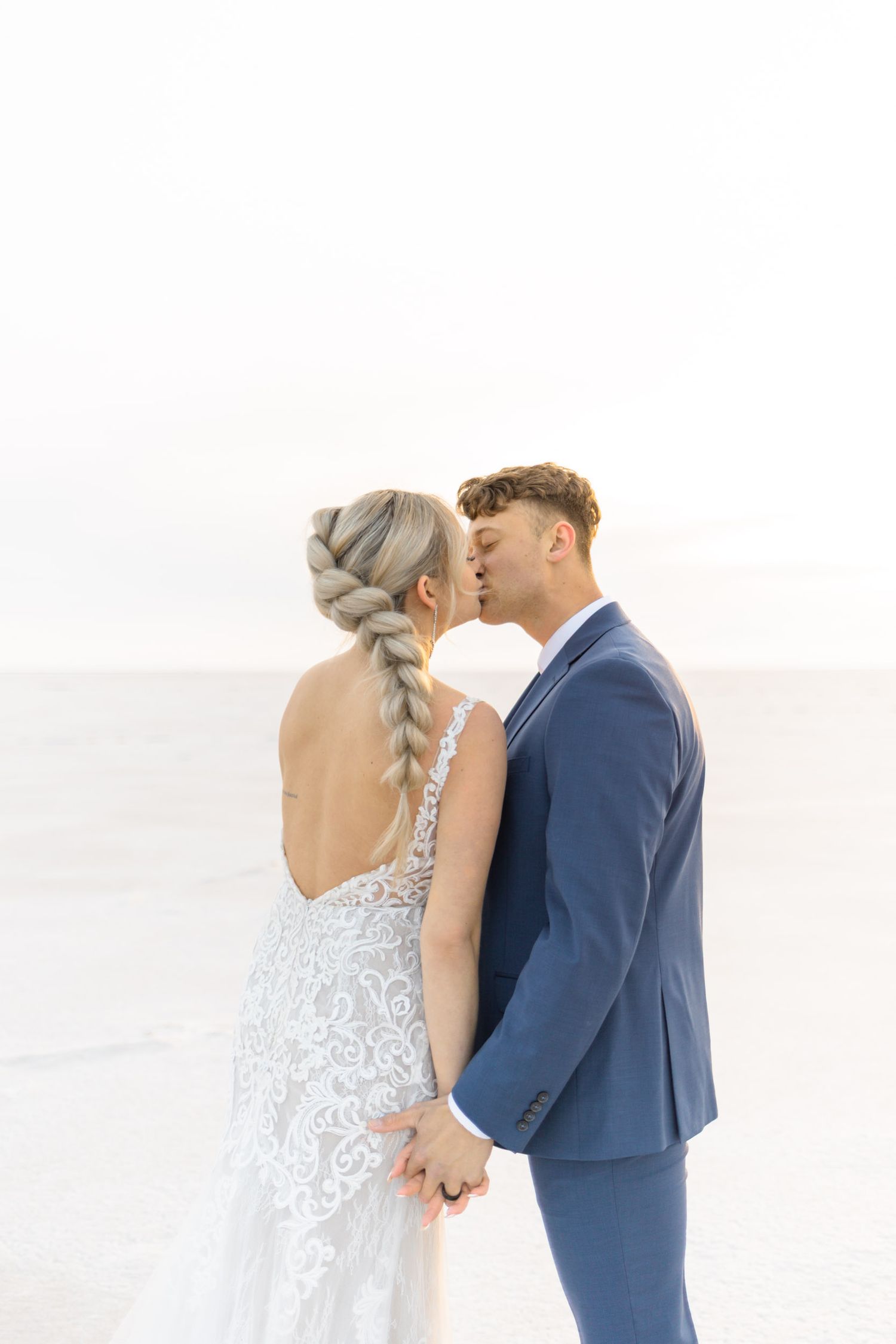 Romantic wedding couple sharing an intimate kiss against a bright white background.