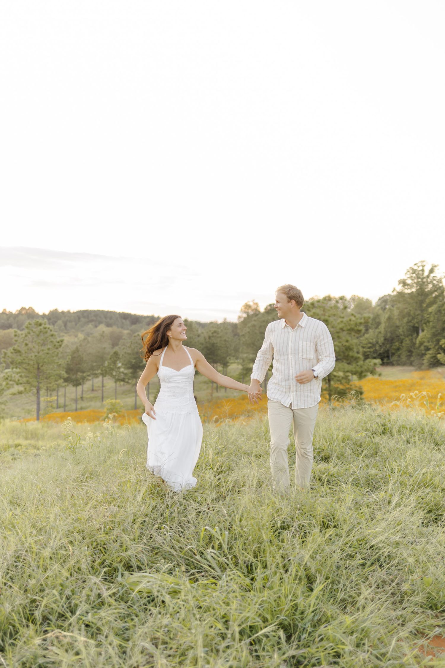 A couple strolls together through a scenic meadow with mountains in the background during engagement session in Chapel Hill, NC.