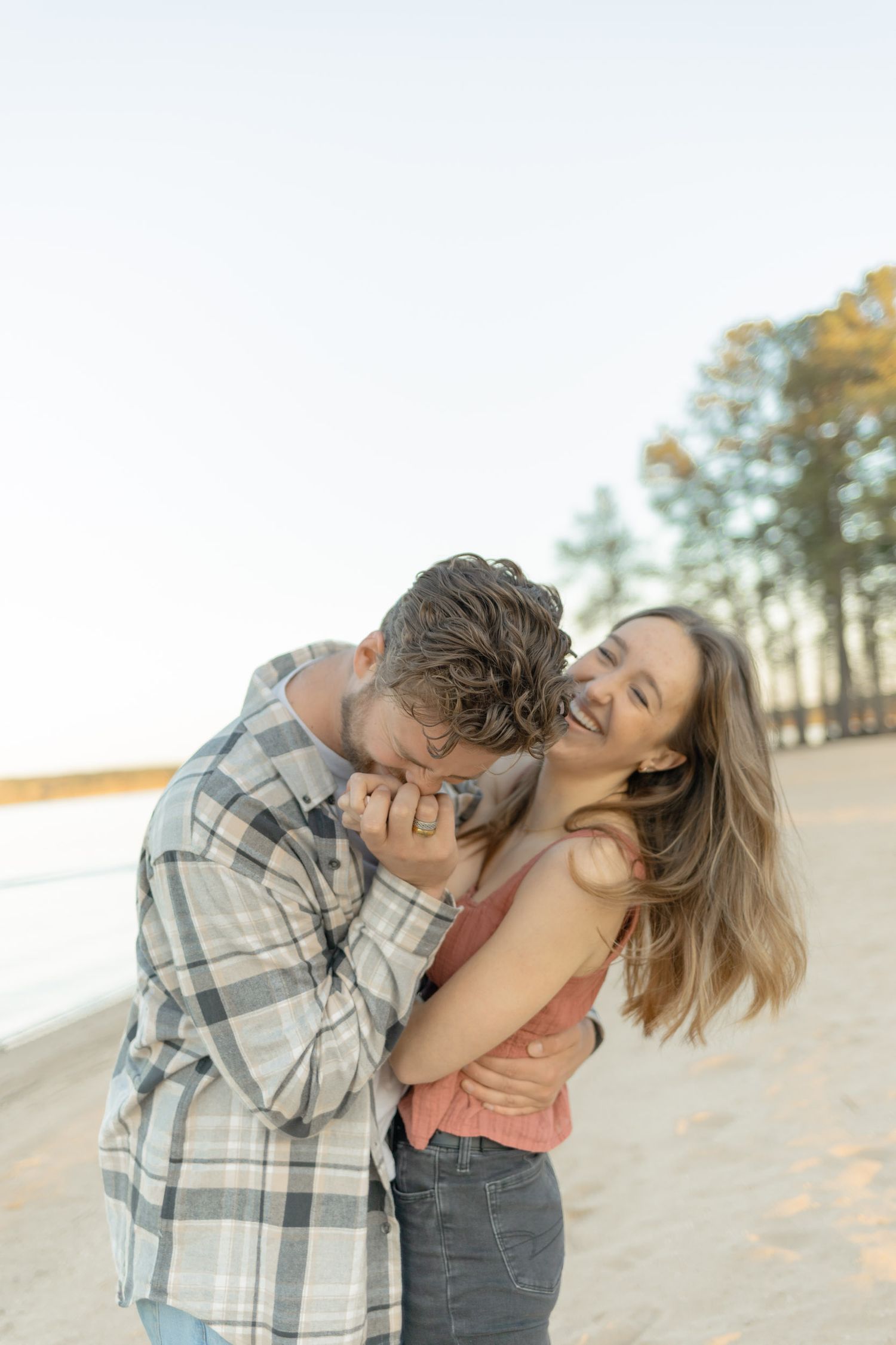 Playful couple in casual clothes sharing an affectionate moment on a sandy beach in Raleigh, North Carolina.