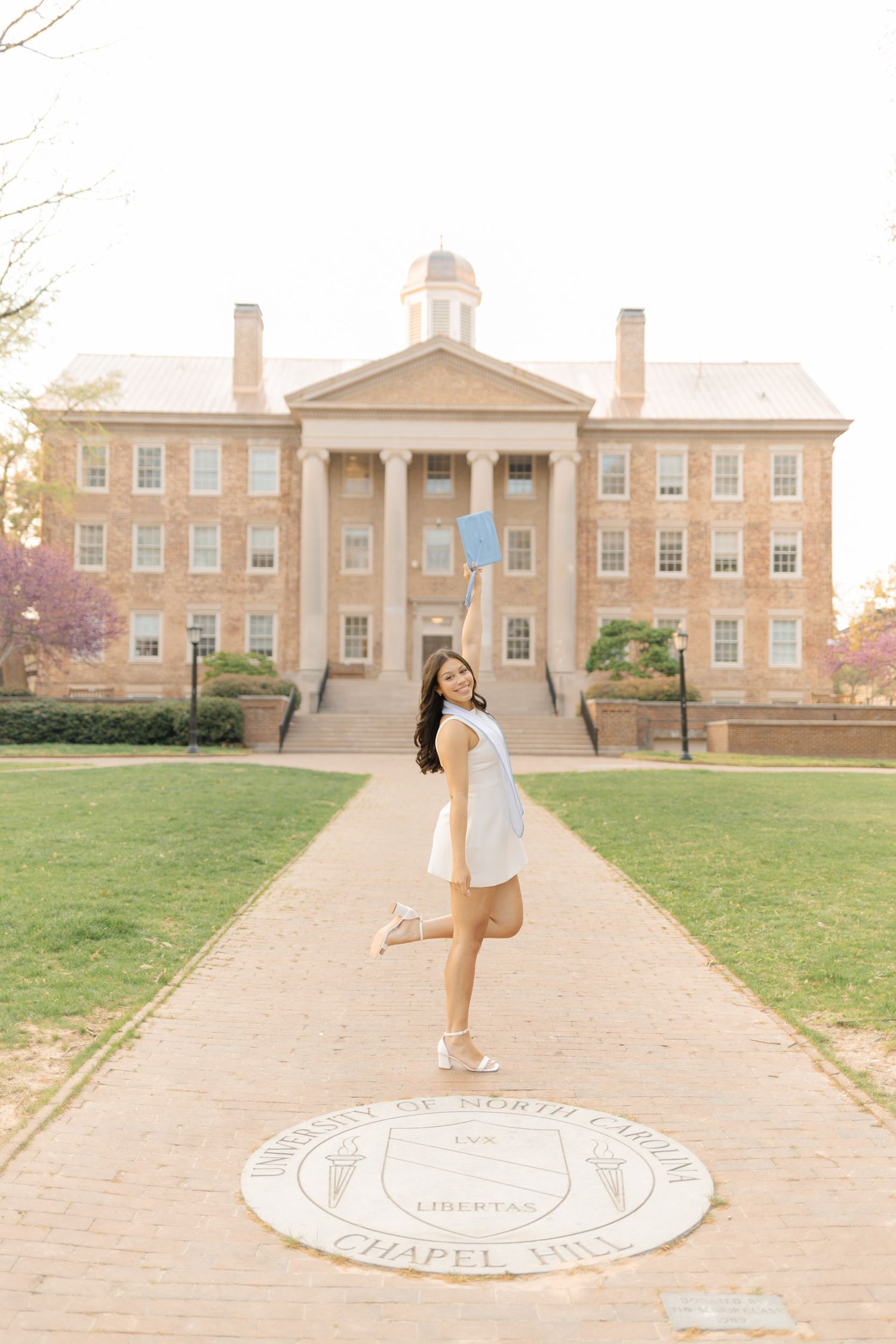 Graduate tossing cap at University of North Carolina Chapel Hill campus seal in front of historic building.