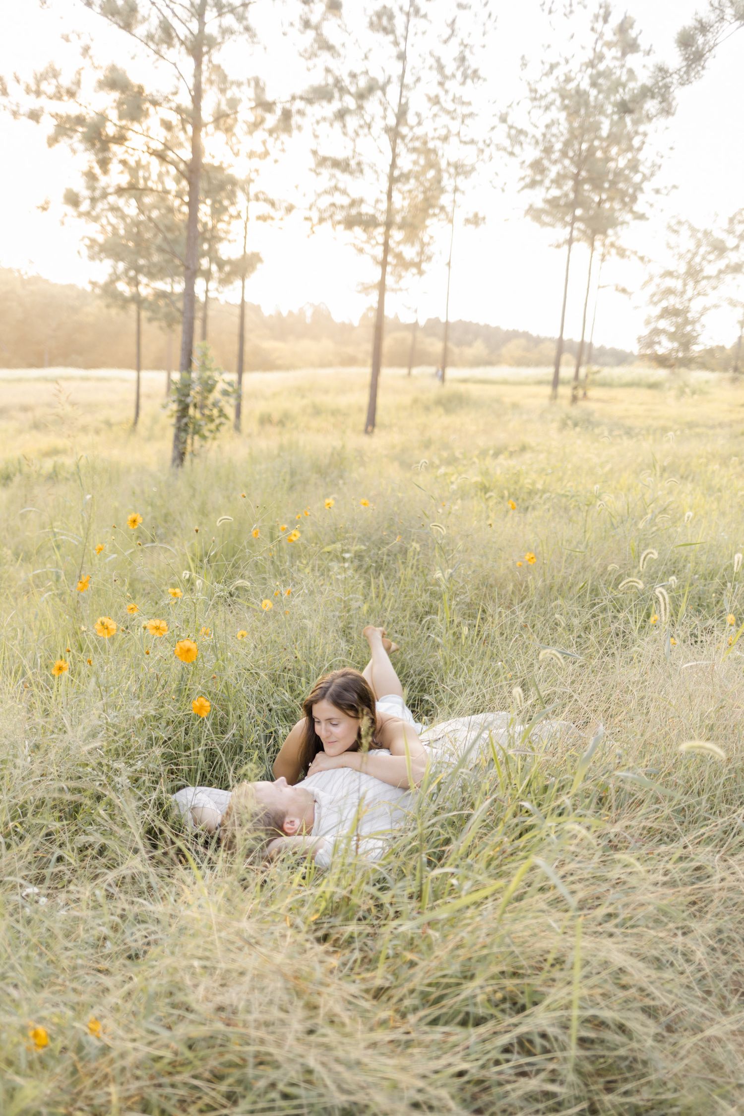 Woman relaxing in a golden sunlit field with wildflowers and tall grass during a warm afternoon.