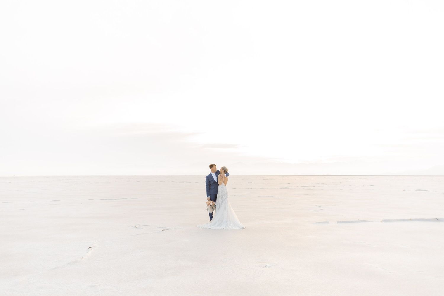 Couple walking on a white sandy beach at sunset with soft pastel colors in the sky during photoshoot at salt flats, utah