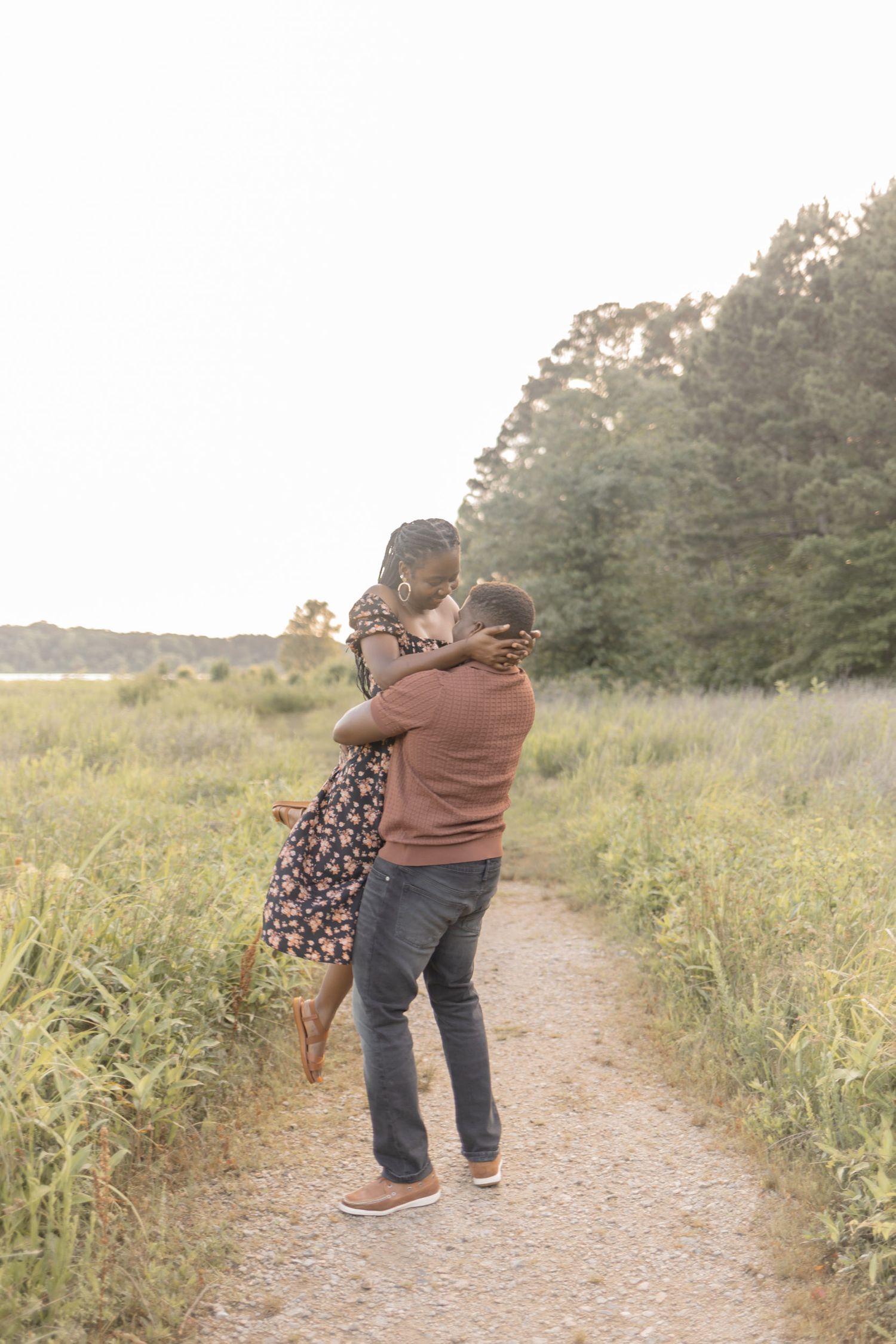 A couple embraces on a nature path, the man lifting the woman in a romantic outdoor engagement photo.
