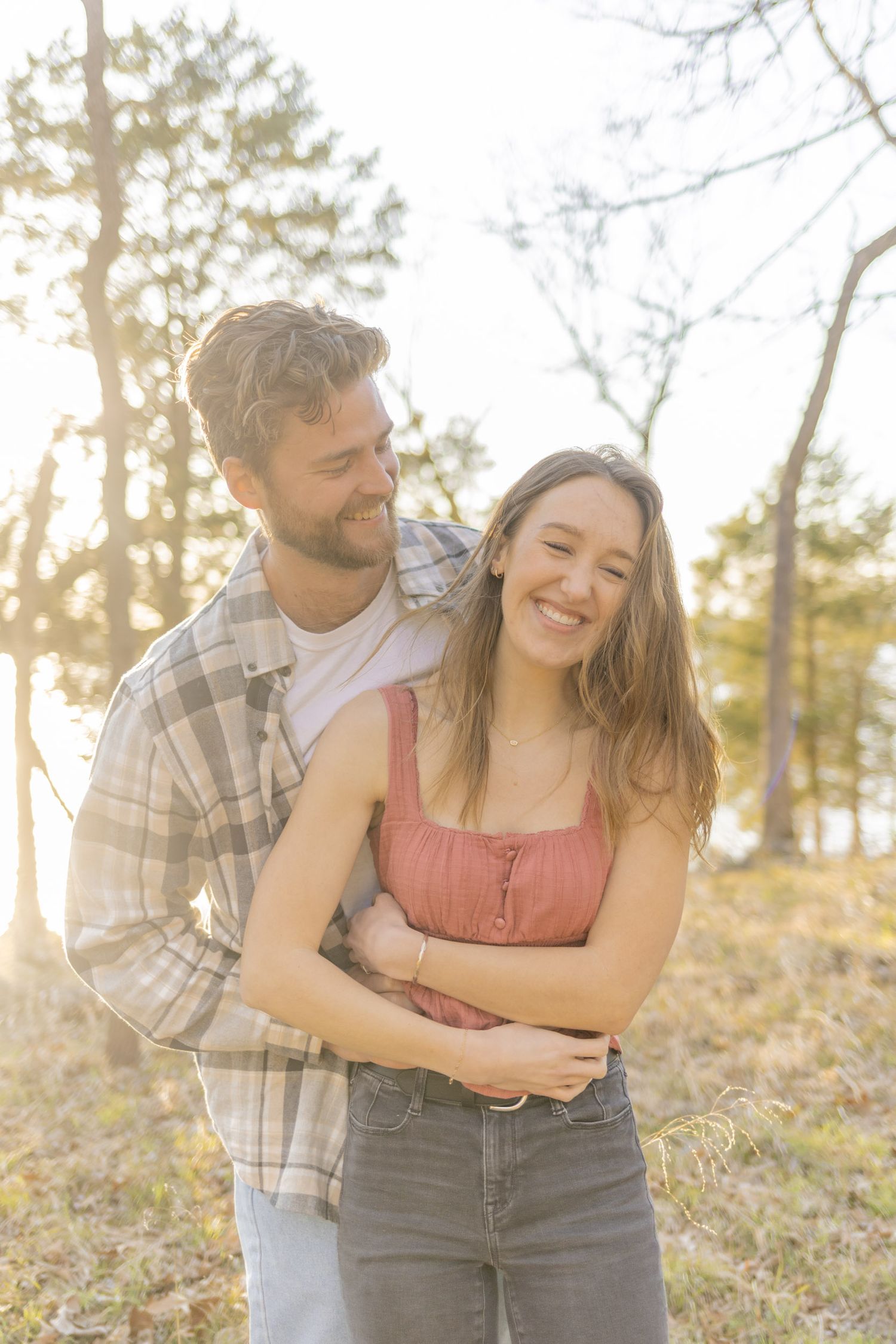 Playful couple laughing together in a wooded area during sunset during photoshoot with Kinsley Nicole Photography.