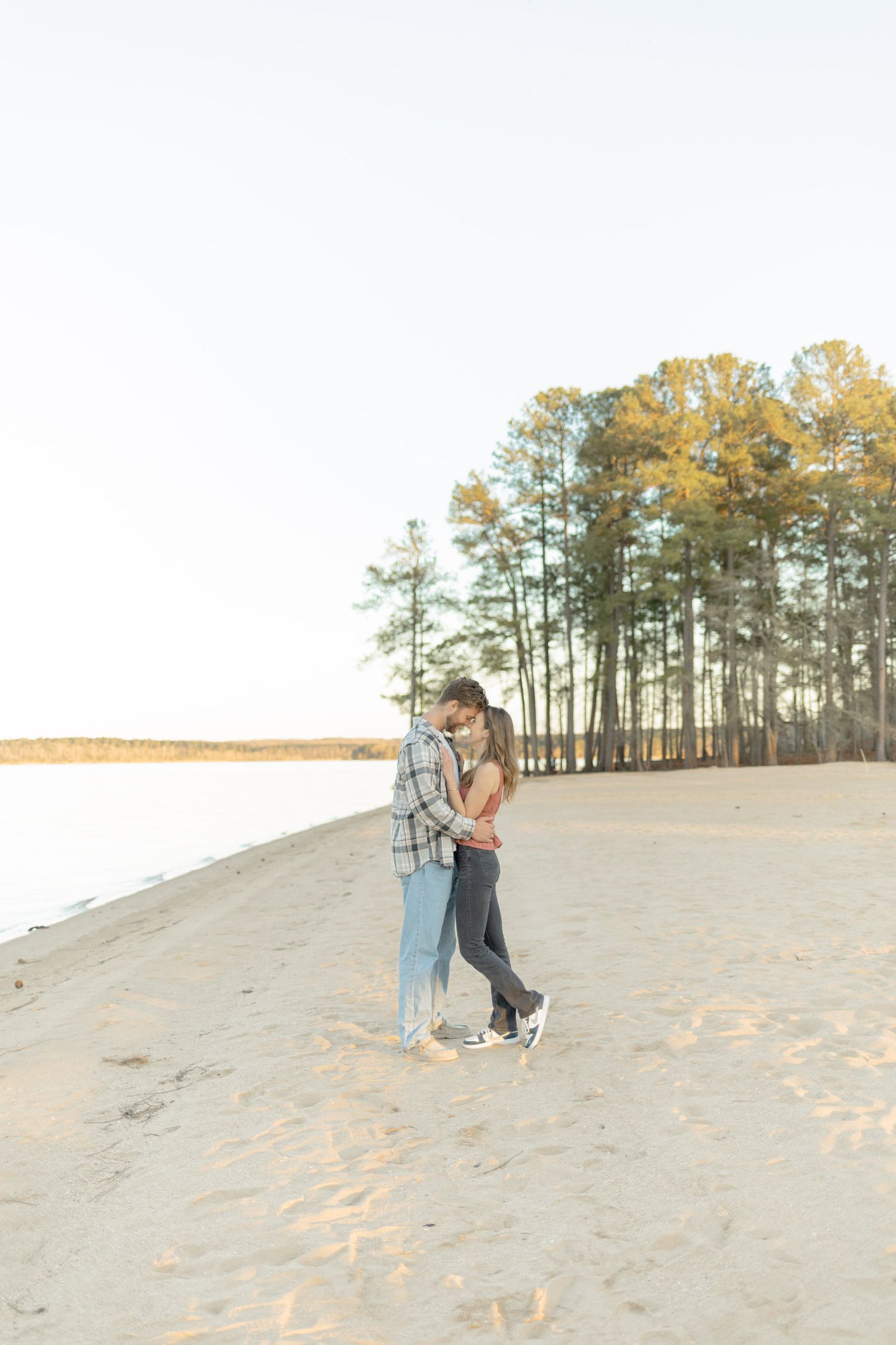 Couple enjoying a romantic moment on sandy dunes with pine trees in distance during photoshoot with Kinsley Nicole Photography.