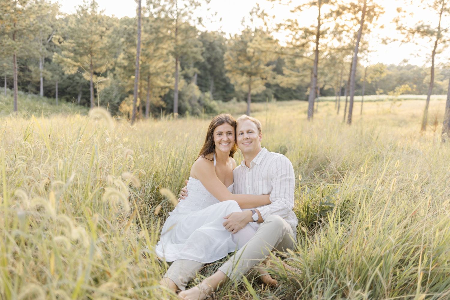 Couple embraces in a sunlit meadow with wildflowers during golden hour during engagement session with photographer in North Carolina.
