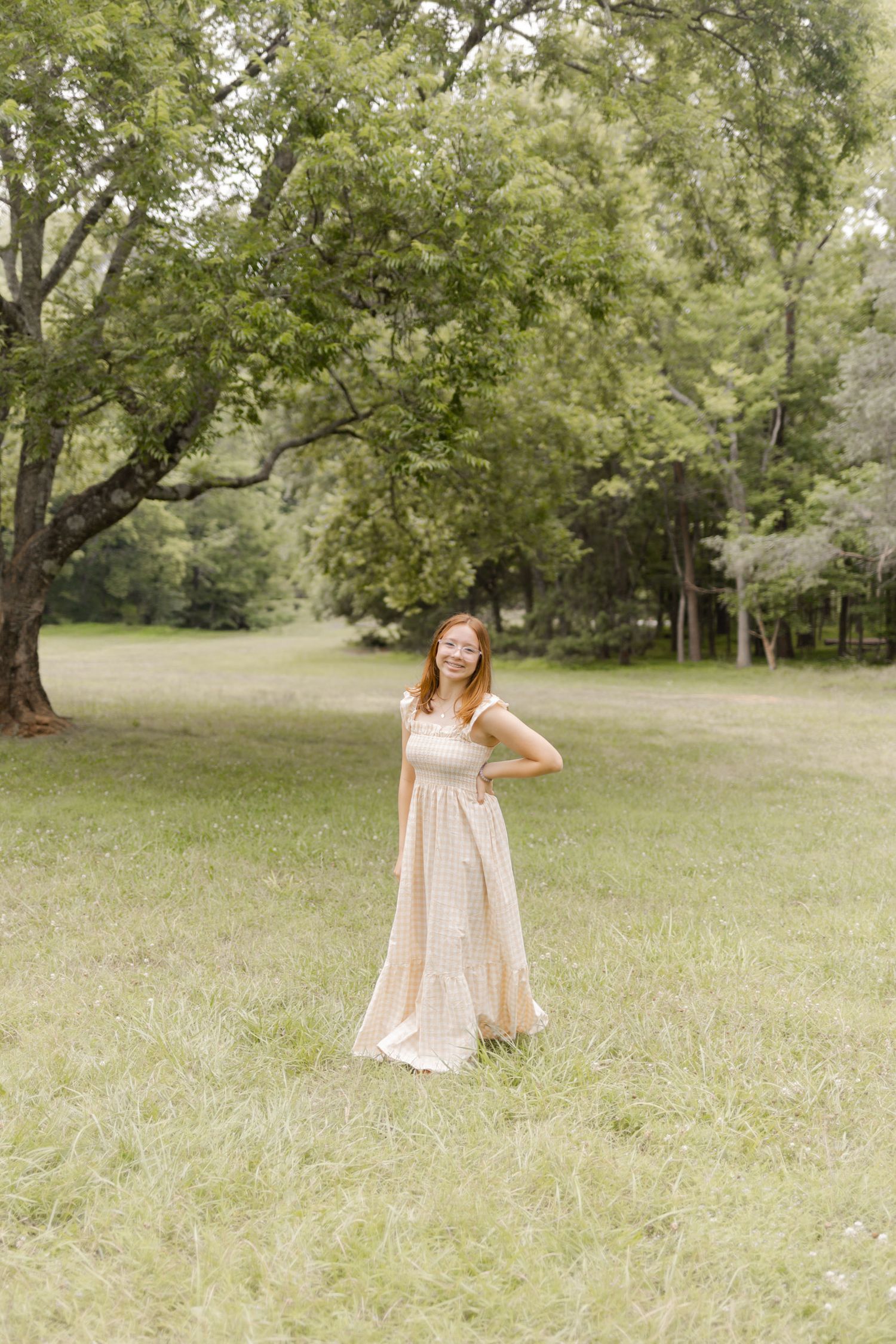 Person in a light-colored dress dances joyfully in a sun-dappled meadow in Durham, North Carolina.