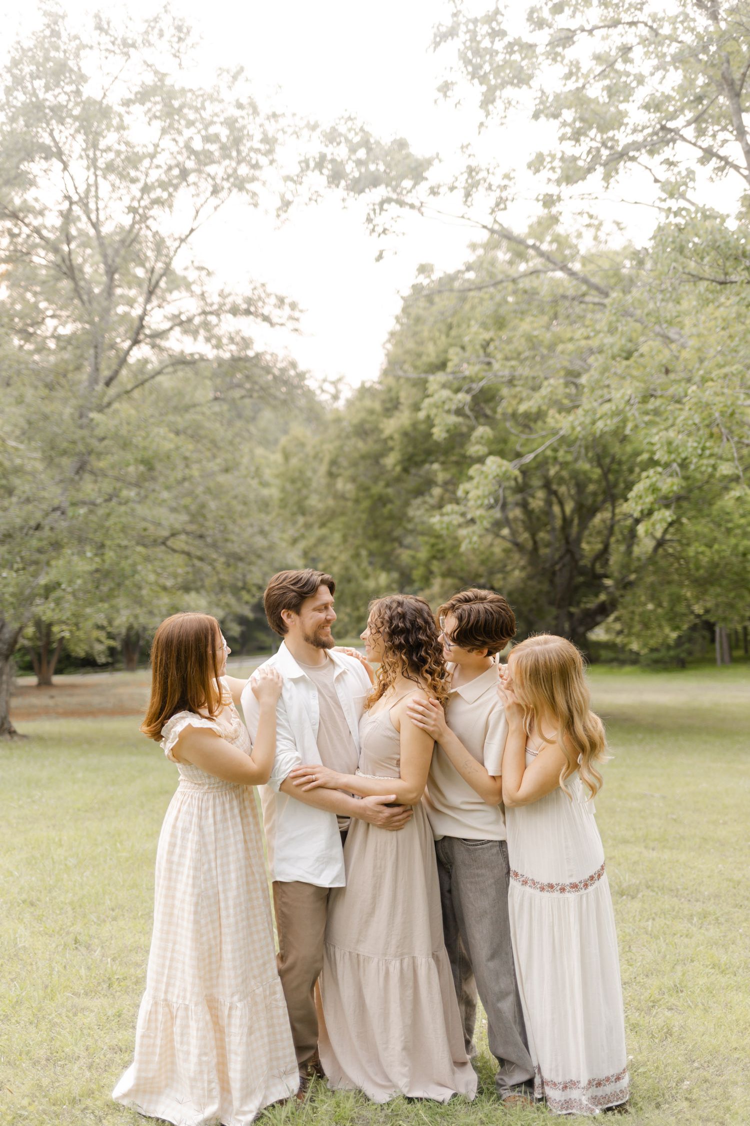 Group hug moment captured in soft lighting as friends gather in a park setting.