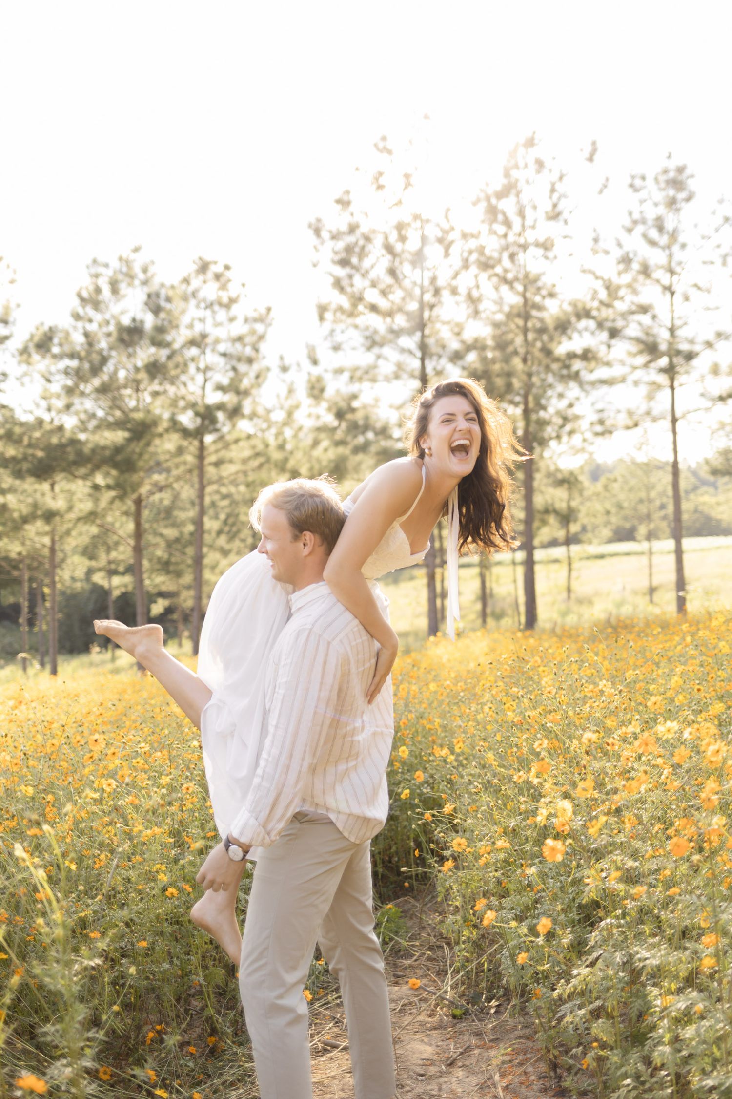 Couple sharing joyful moments in a sunlit meadow filled with yellow wildflowers during golden hour for engagement photoshoot in Chapel Hill.