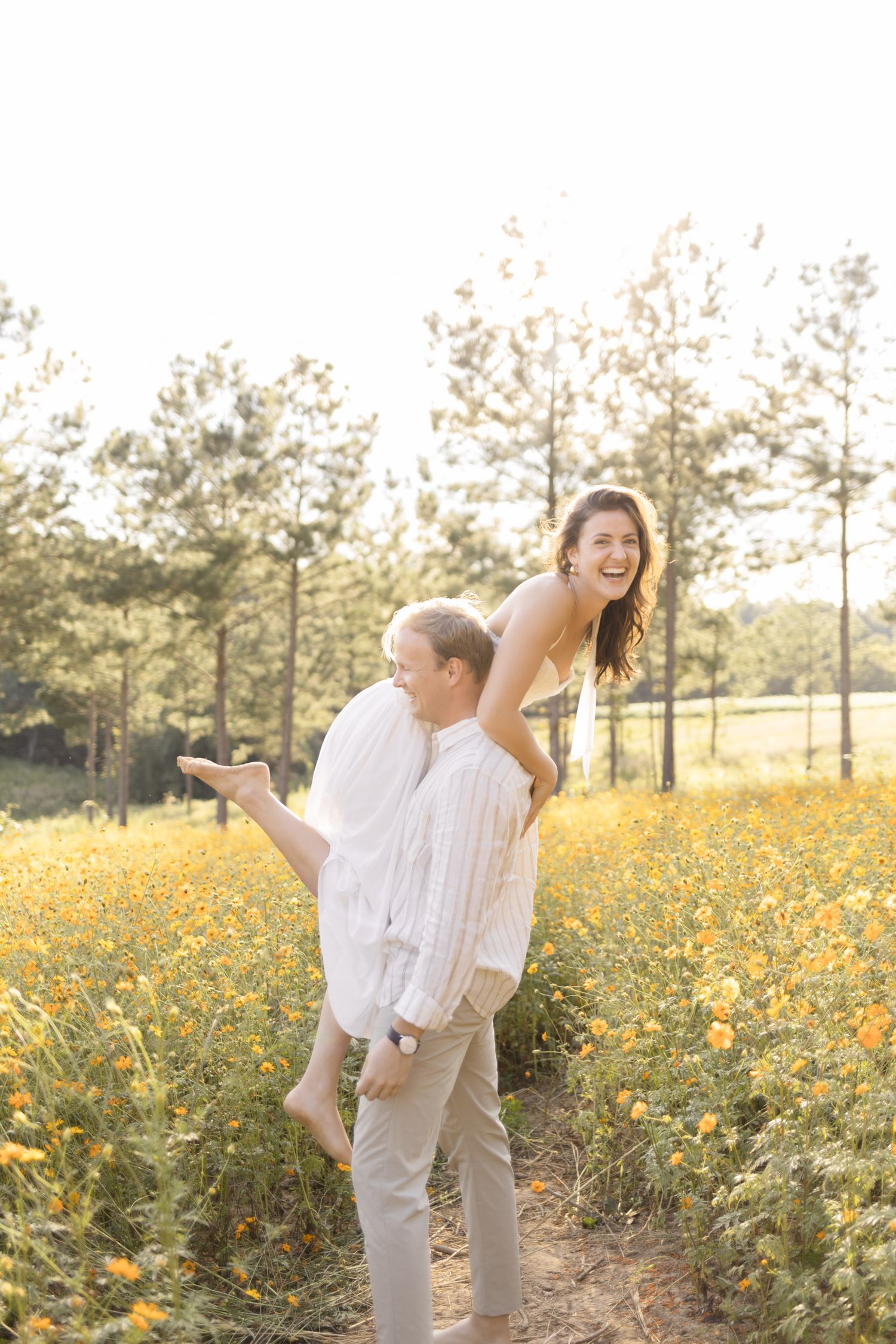 Couple dancing and laughing together in a sunlit meadow filled with yellow wildflowers during lifestyle portrait photoshoot.